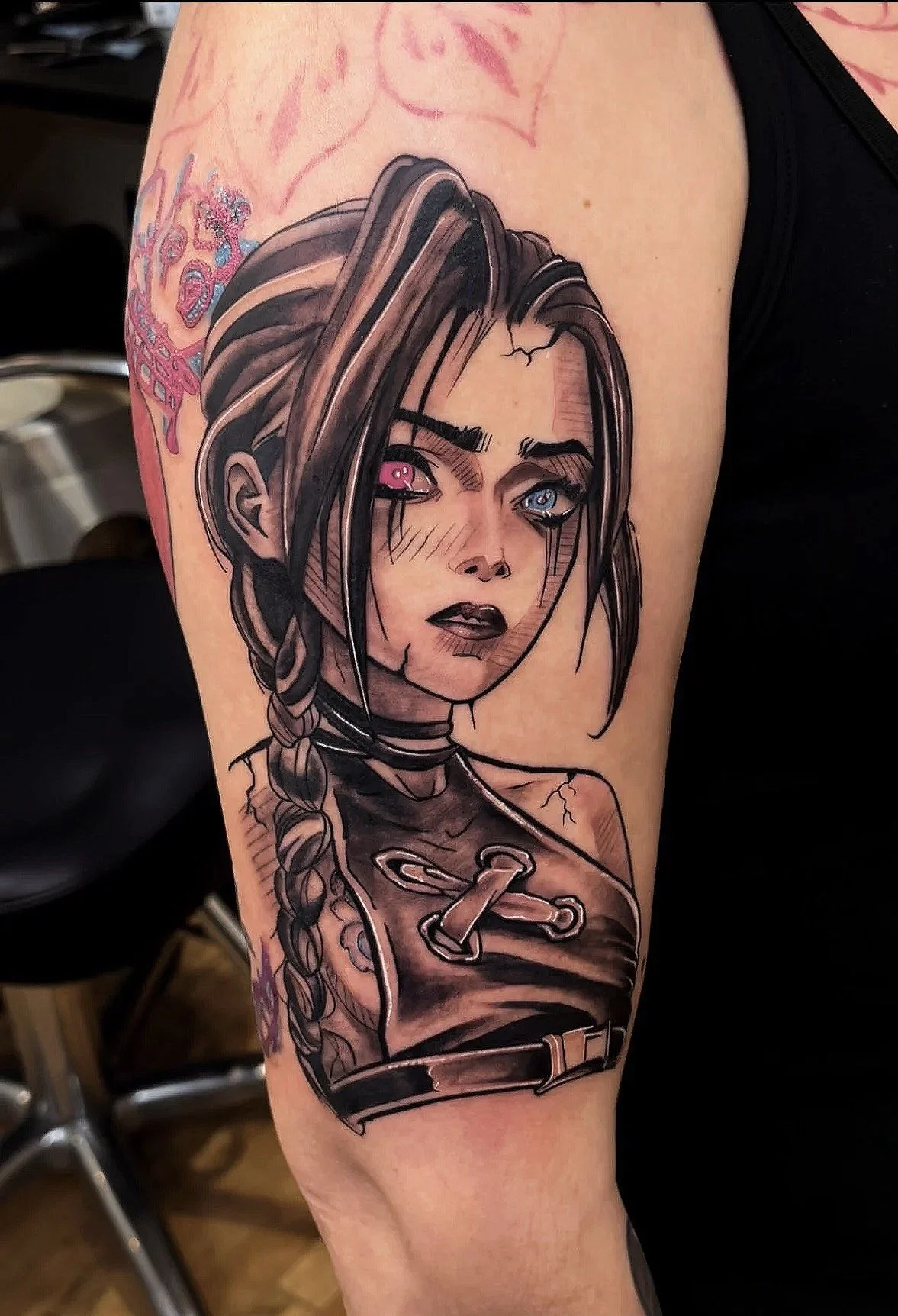 Black and gray tattoo of a female character with long braided hair, one eye pink and the other blue, wearing a dark outfit with a collar and hook-shaped accessory, with cracks and shading to create a dramatic effect.