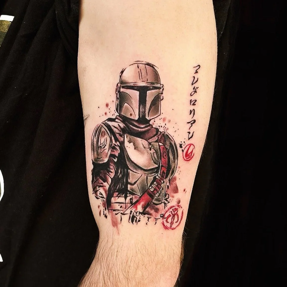 Tattoo of a Mandalorian character from Star Wars wearing armor and a helmet, with red ink accents and script writing.