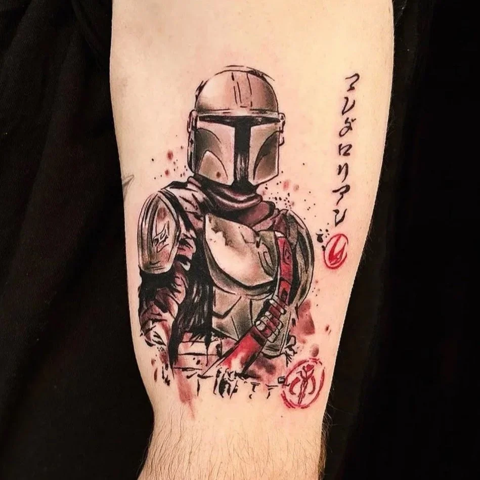 Tattoo of a Mandalorian character from Star Wars wearing armor and a helmet, with red ink accents and script writing.