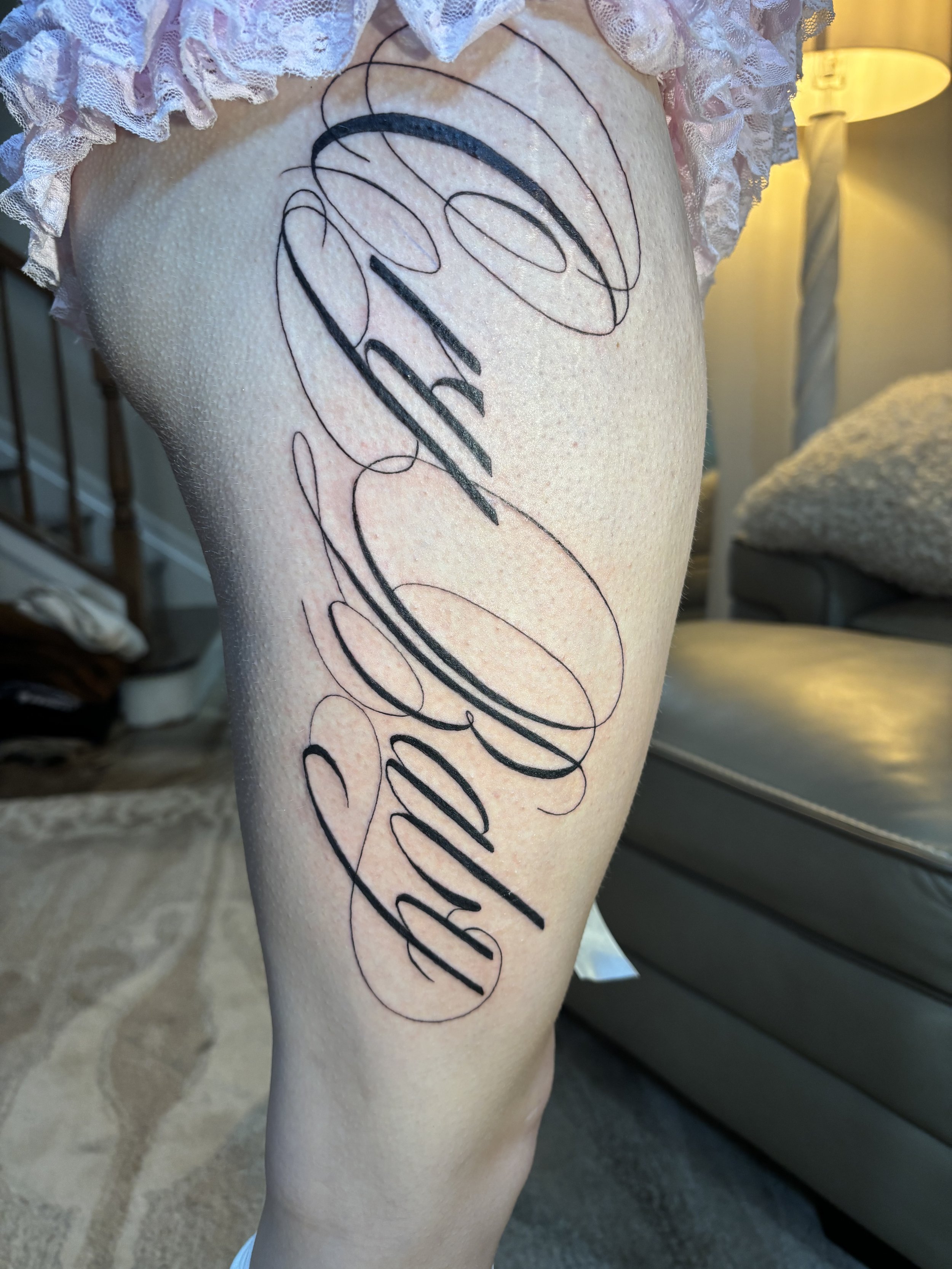 Close-up of a person's thigh with a large tattoo featuring the word 'cry baby' written in elegant, flowing cursive script.