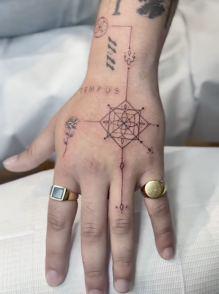 Detailed geometric tattoo on a person's hand with lines, circles, and a sacred geometric pattern, alongside small symbols and the word 'TEMPUS'