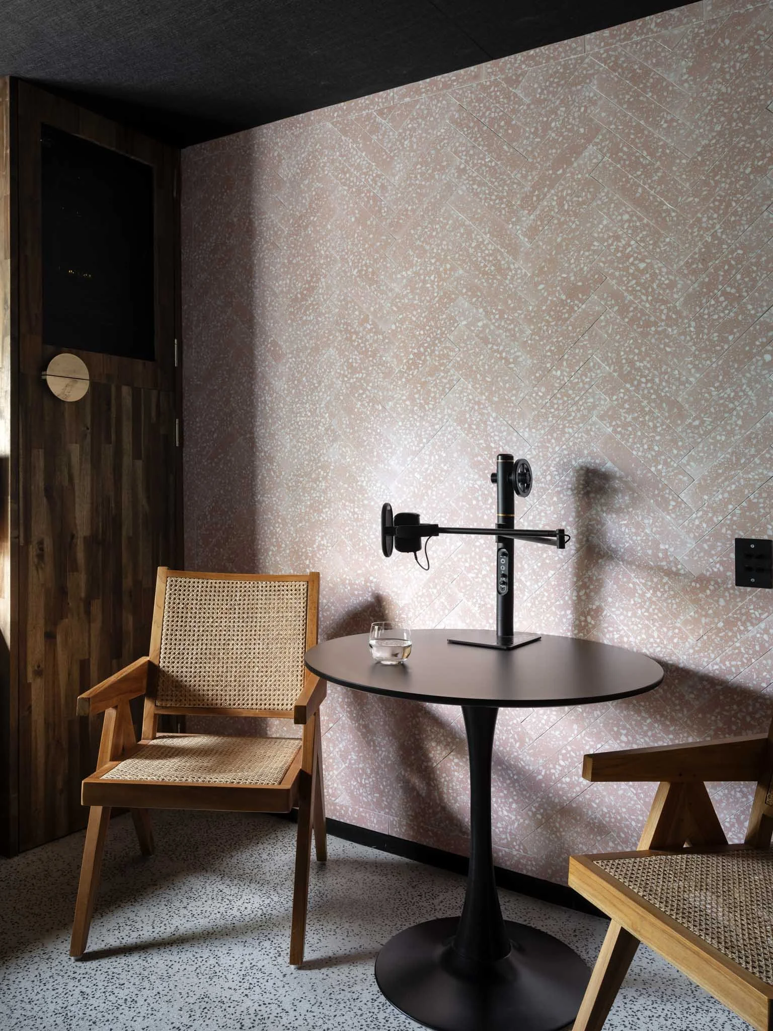 Interior of a room with two wooden chairs, a small round table, and a fitness device on the table, against a pink speckled wall.