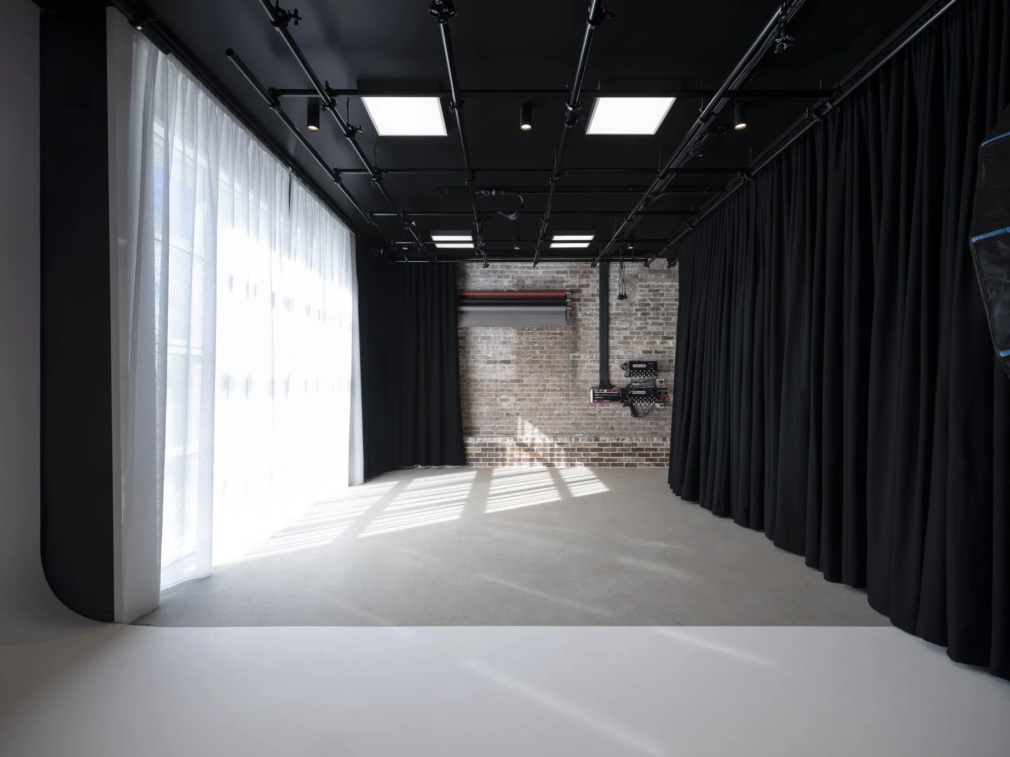 Empty photography or video studio with black curtains, white curtains, brick wall, and overhead lighting.