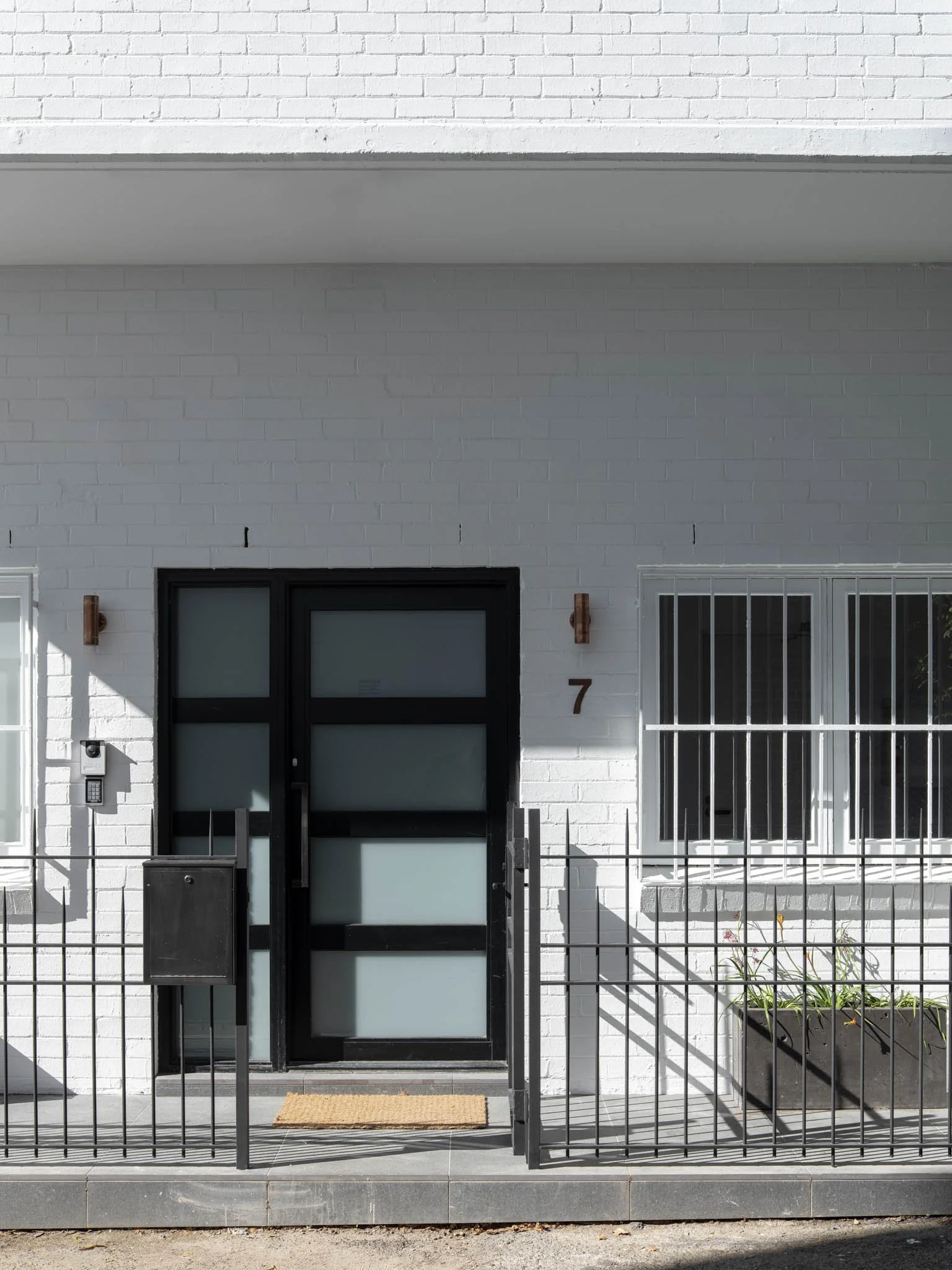 Modern white brick house with black door and window, number 7, and a metal fence in front.