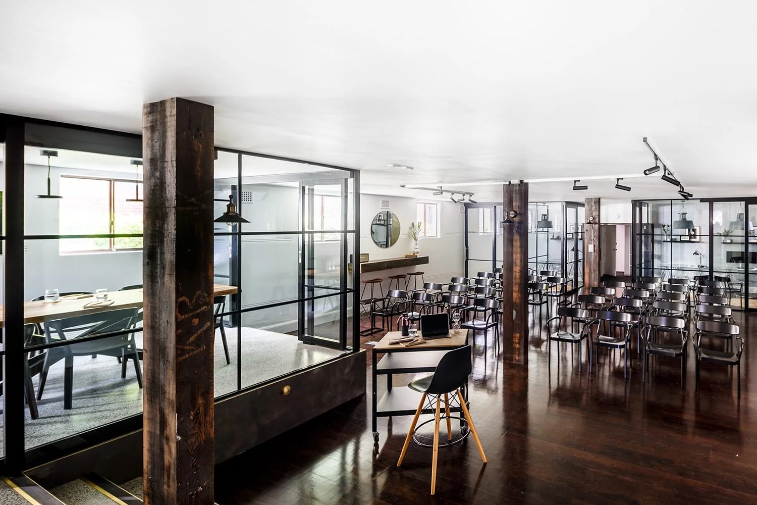 Modern event space with wooden floors, glass-walled rooms, and rows of black chairs for seating.