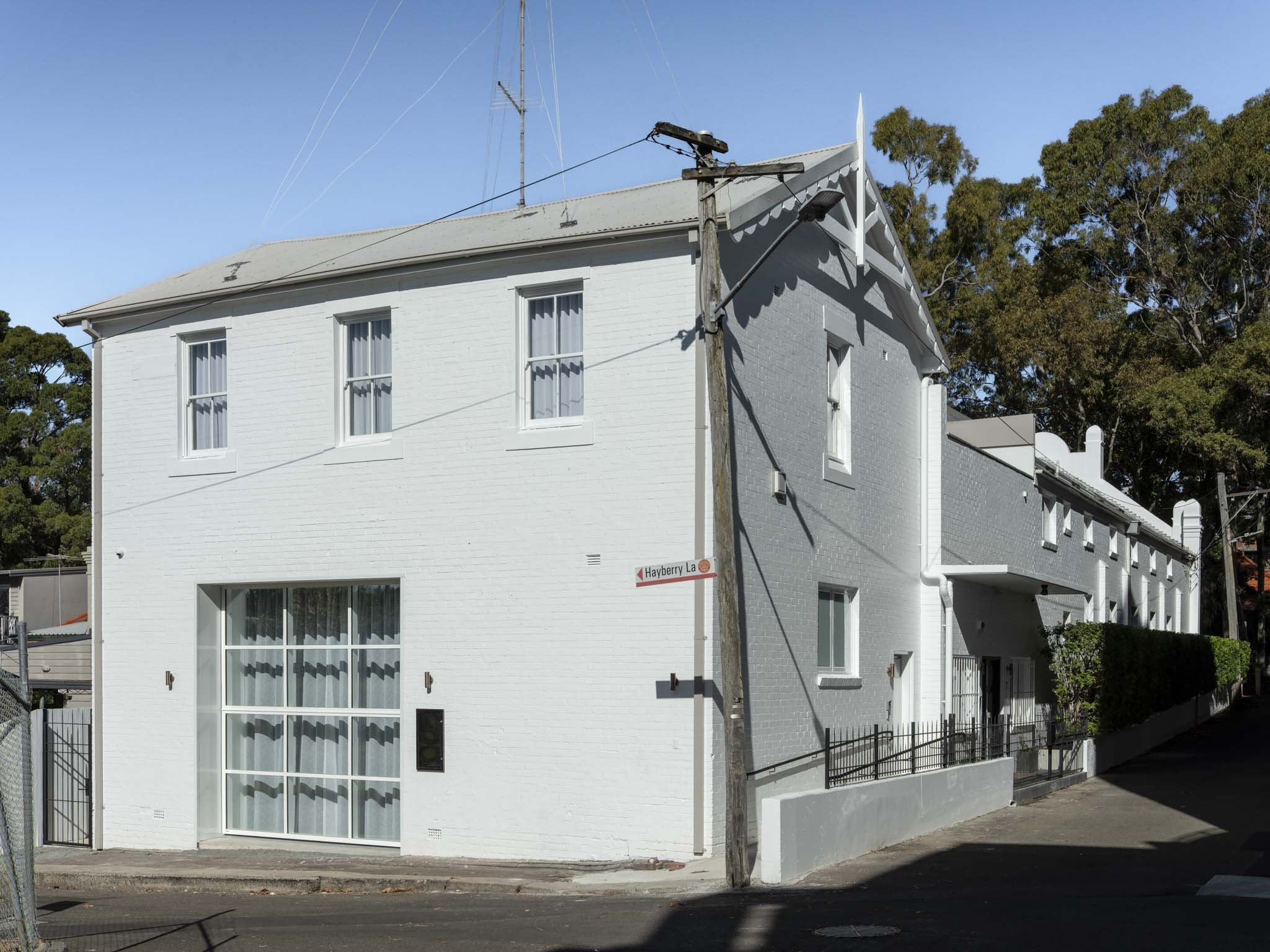 A three-story white and gray brick building with multiple windows, a garage door, and a street sign that reads 'Hayberry La.'