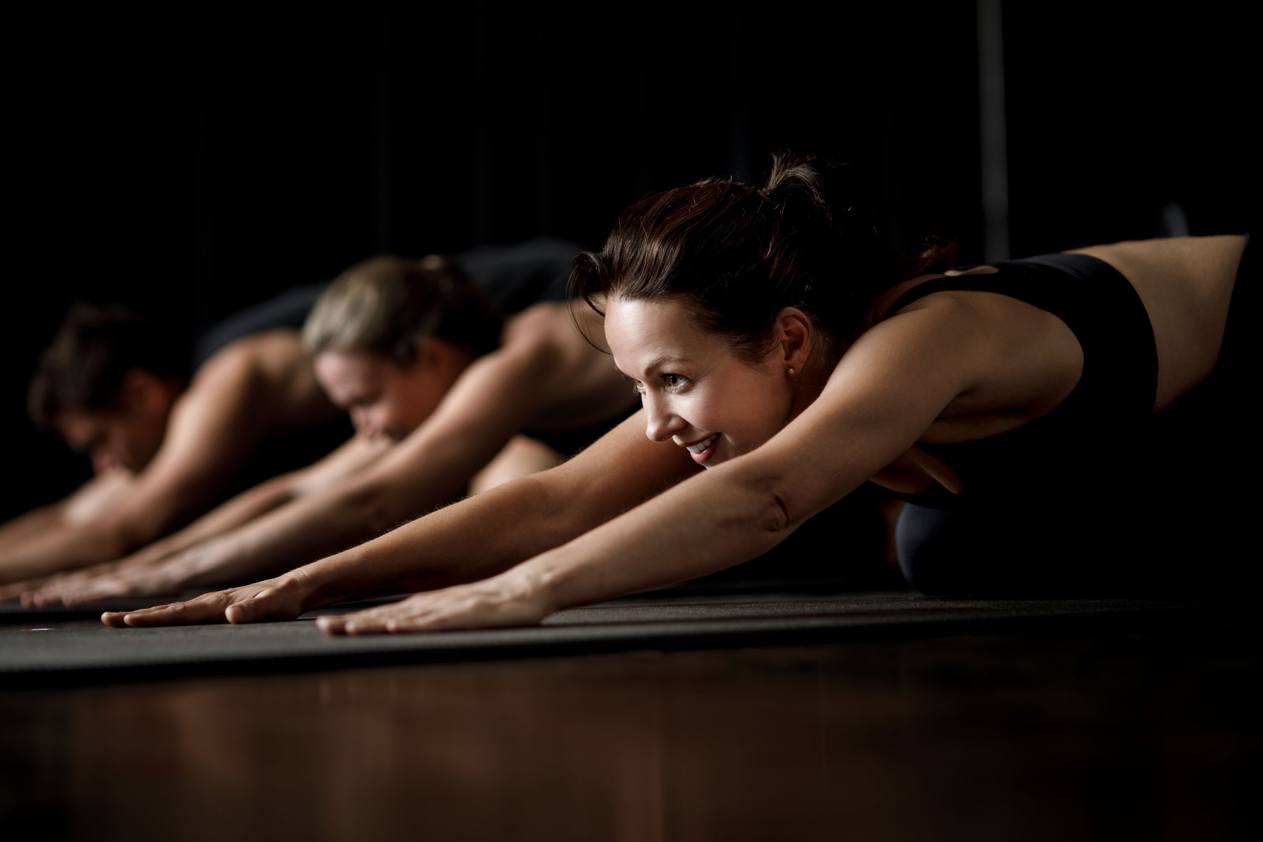Women doing yoga stretch exercise in a row on yoga mats.