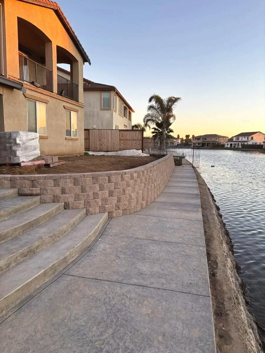 Newly constructed outdoor patio with stairs, retaining wall, and sidewalk along a waterway at sunset, in a residential neighborhood.