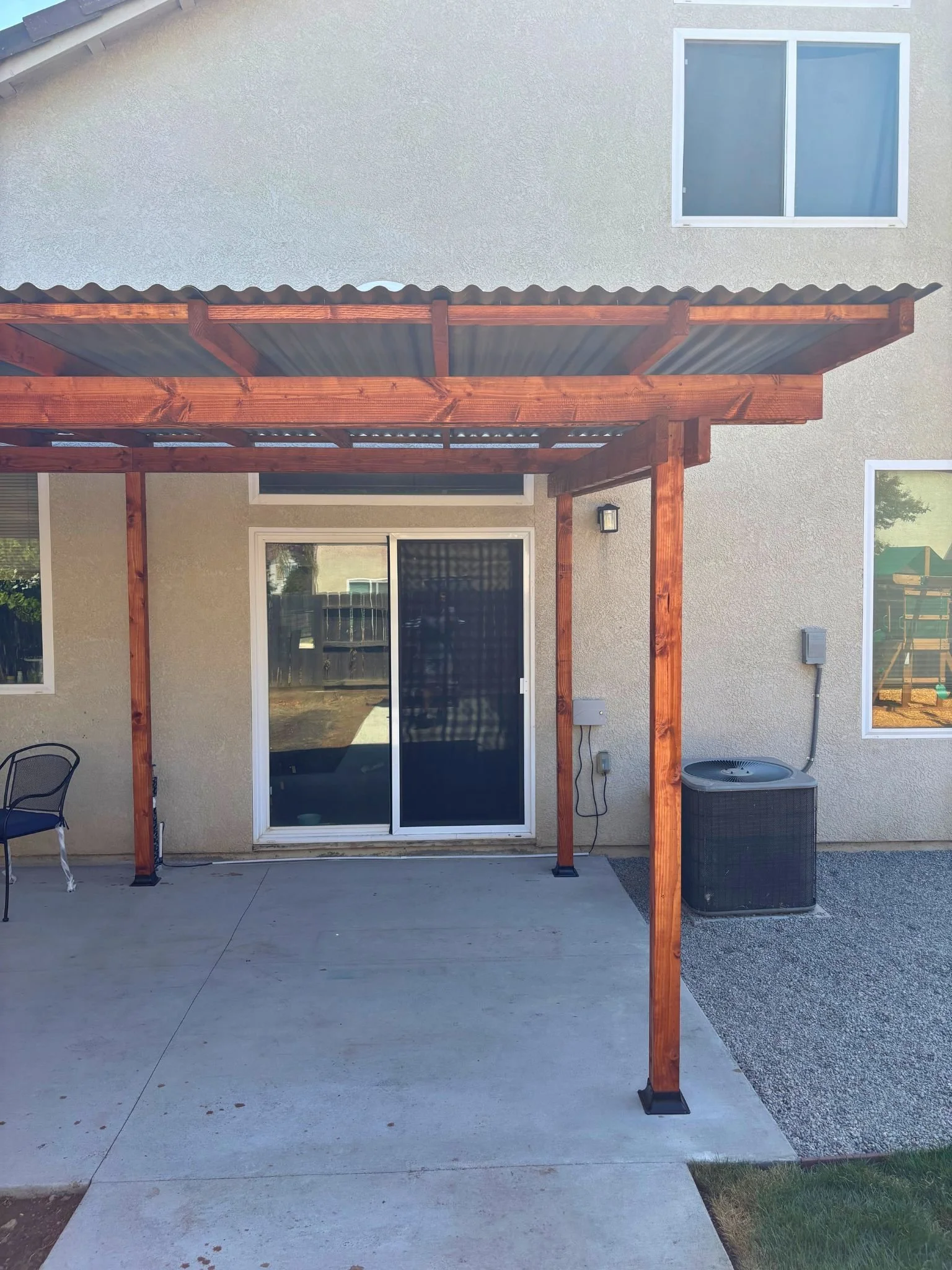 Backyard patio with a wooden frame for a future roof or cover, a sliding glass door, a window, and an air conditioning unit against the house wall.