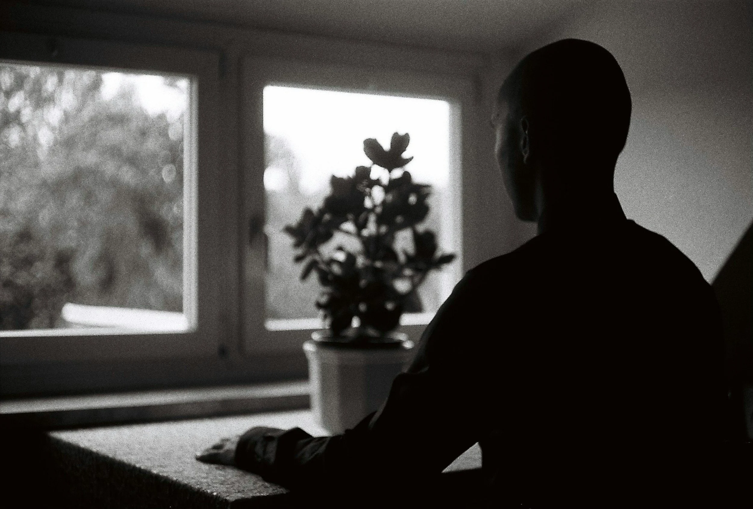 Man sitting quietly at a kitchen table with work left unfinished, illustrating how overworking and constant busyness can become a trauma response and survival strategy.
