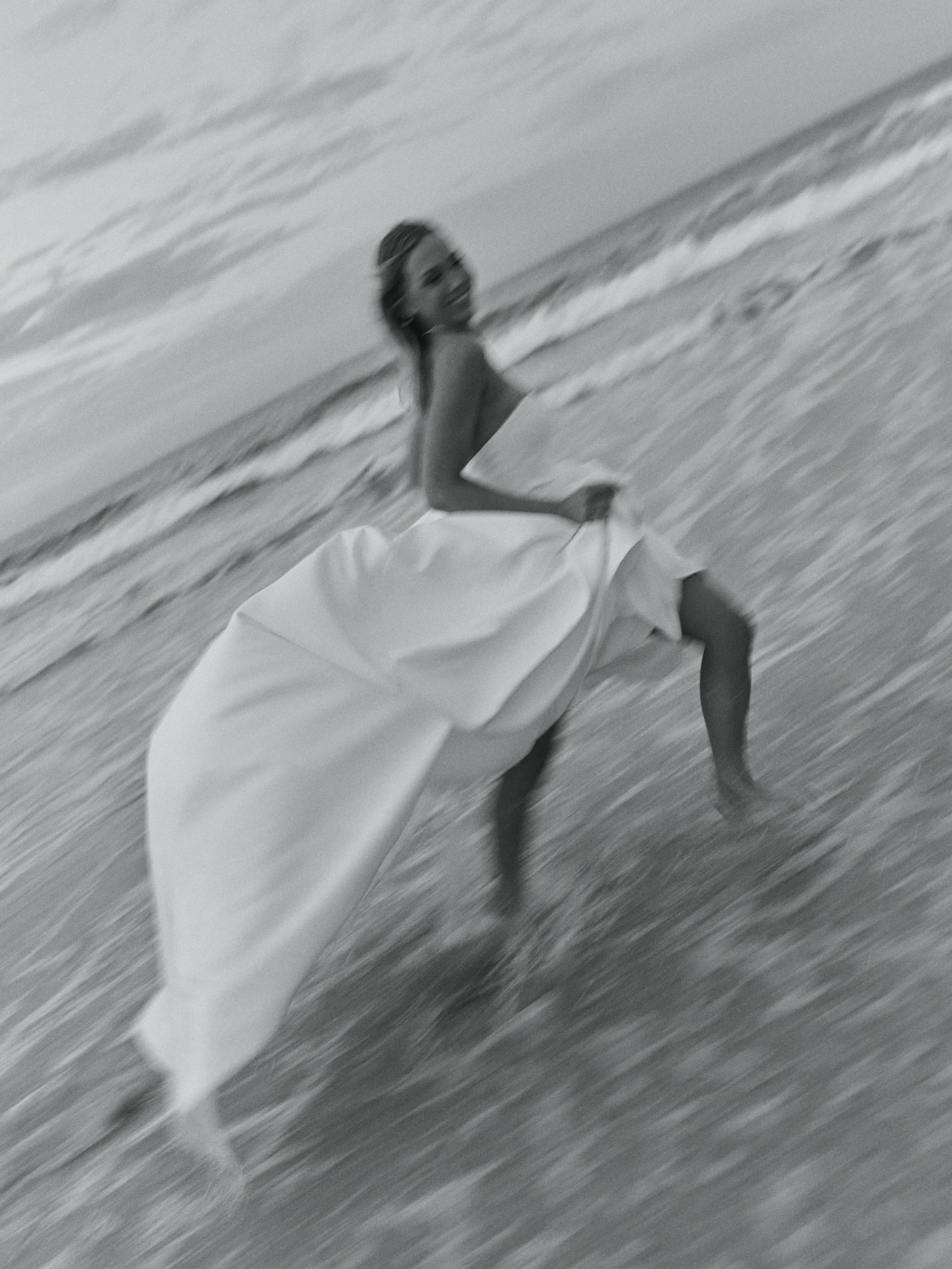 A woman in a wedding dress standing in the ocean with waves around her, in black and white.
