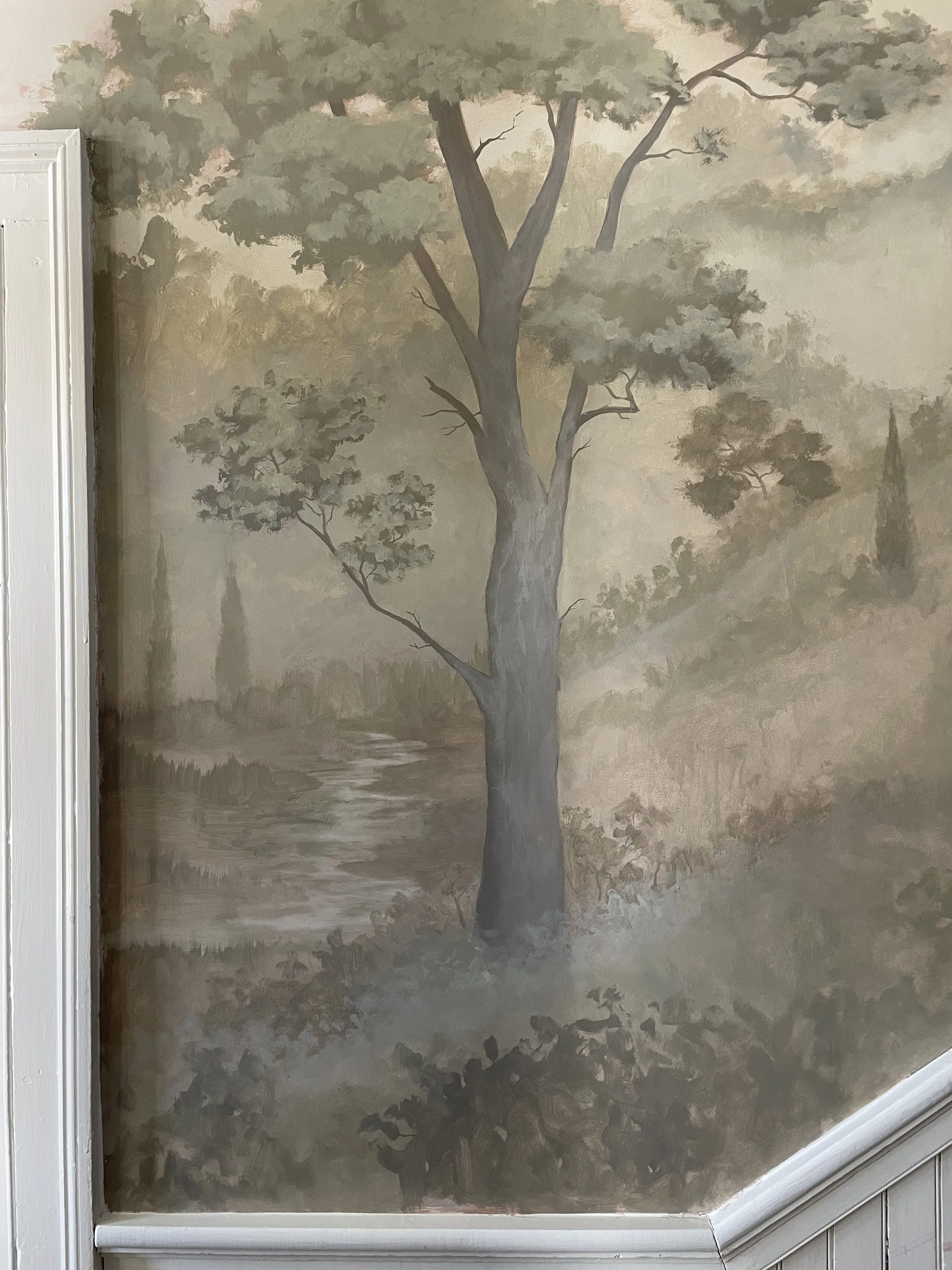 A mural of a natural landscape featuring a large tree with a thick trunk and green foliage, a small stream, and distant trees in muted green and brown tones.