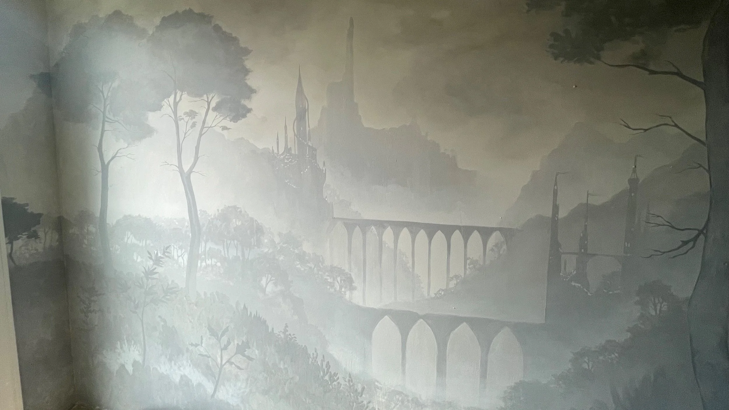 Fantasy landscape mural with a castle on a mountain, waterfalls, and trees in muted shades of green and gray by Charleston, SC based fine art muralist Gabrielle Hasenstab.