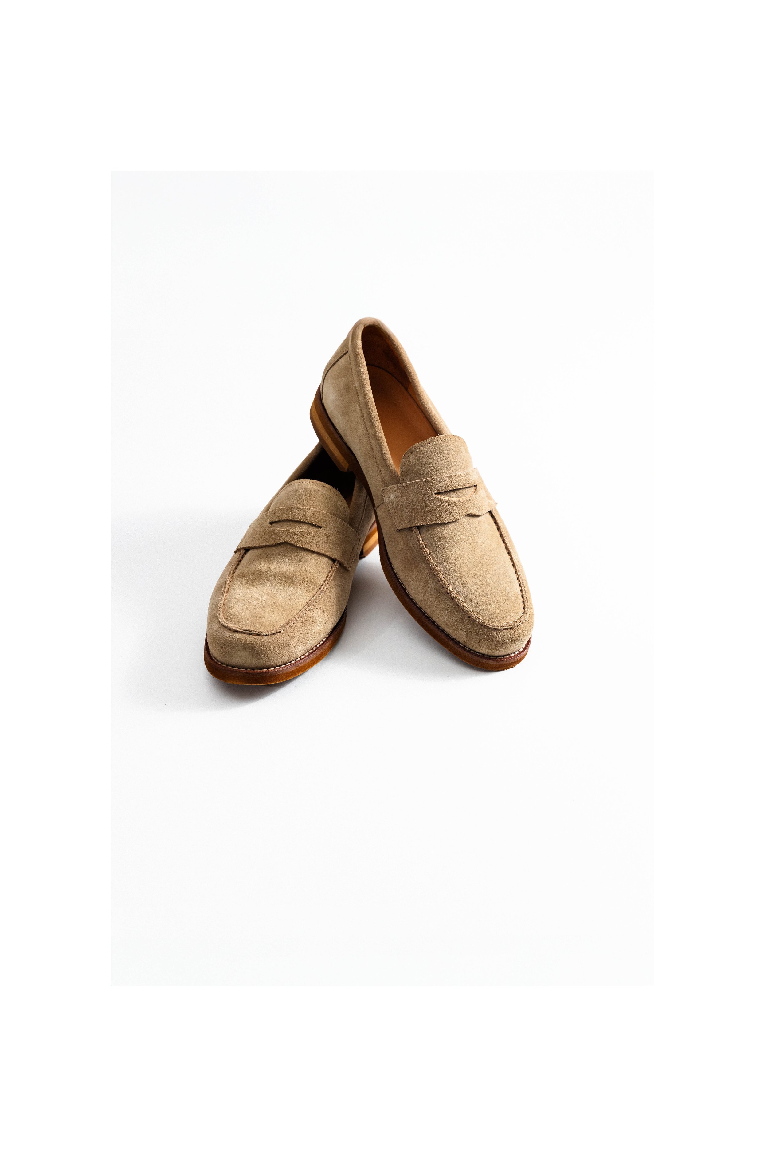 Beige suede loafers with a strap across the top, positioned on a white background.