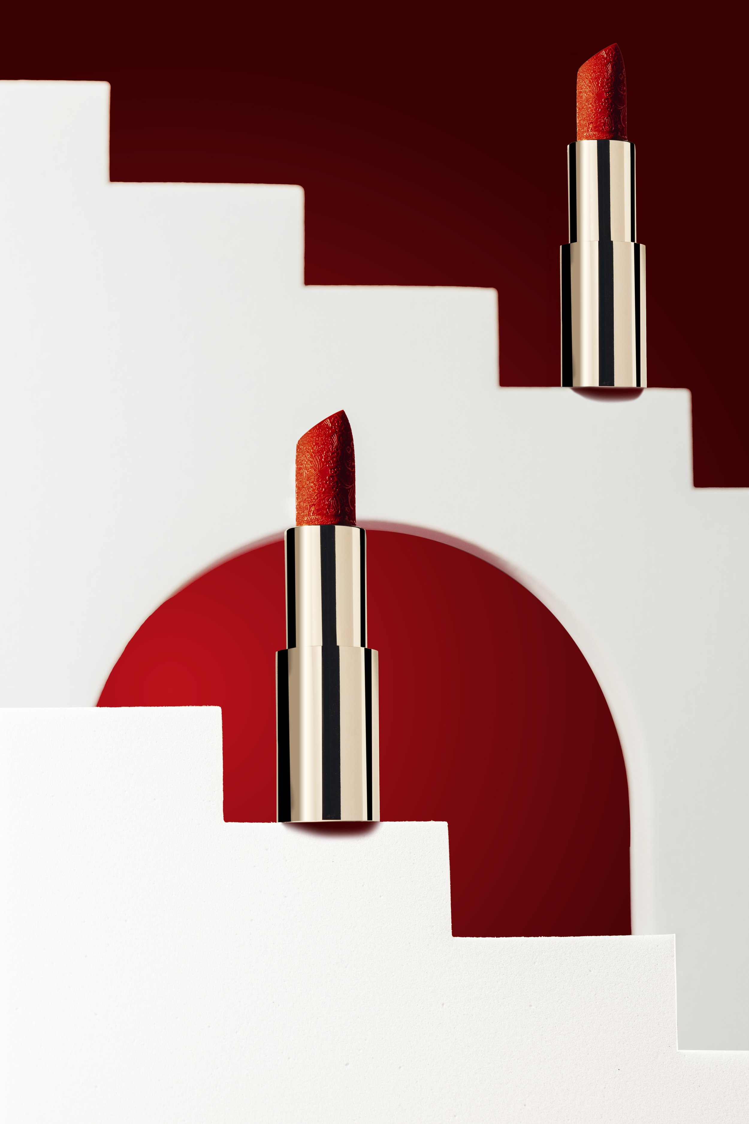 Red lipstick tubes on white geometric stands with a red background.