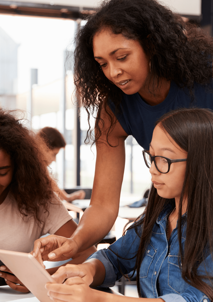 A teacher helping a student with an electronic device in a classroom.