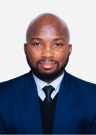 Headshot of a man with a shaved head, beard, and mustache, wearing a dark blue suit, white shirt, and dark tie against a plain white background.