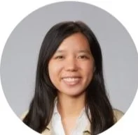 A young woman with long dark hair smiling, wearing a white shirt, in front of a gray circular background.