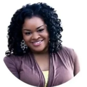 A woman with curly black hair smiling, wearing a mauve jacket and silver earrings.