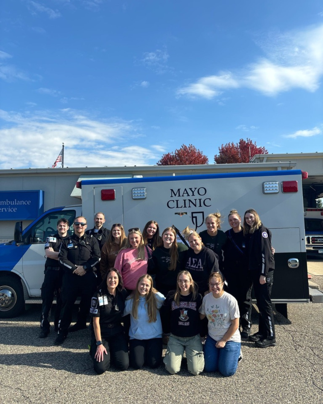 Group of five young women standing behind a kitchen counter, smiling. They are likely participating in a cooking or baking activity in a kitchen with wooden cabinets and modern appliances.