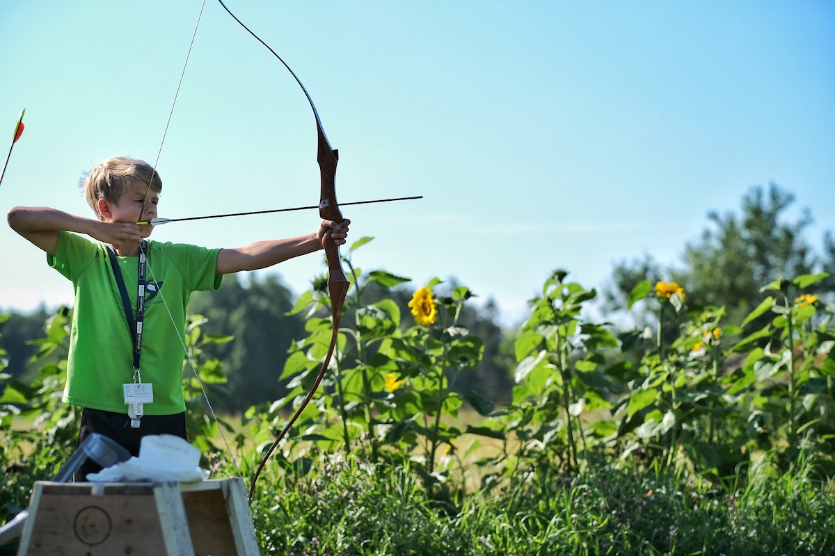 En gutt skyter med bue i en åker med solroser.