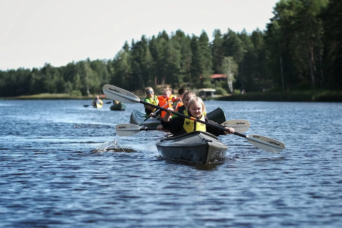 En gruppe barn som padler kano på en rolig innsjø omgitt av skog.