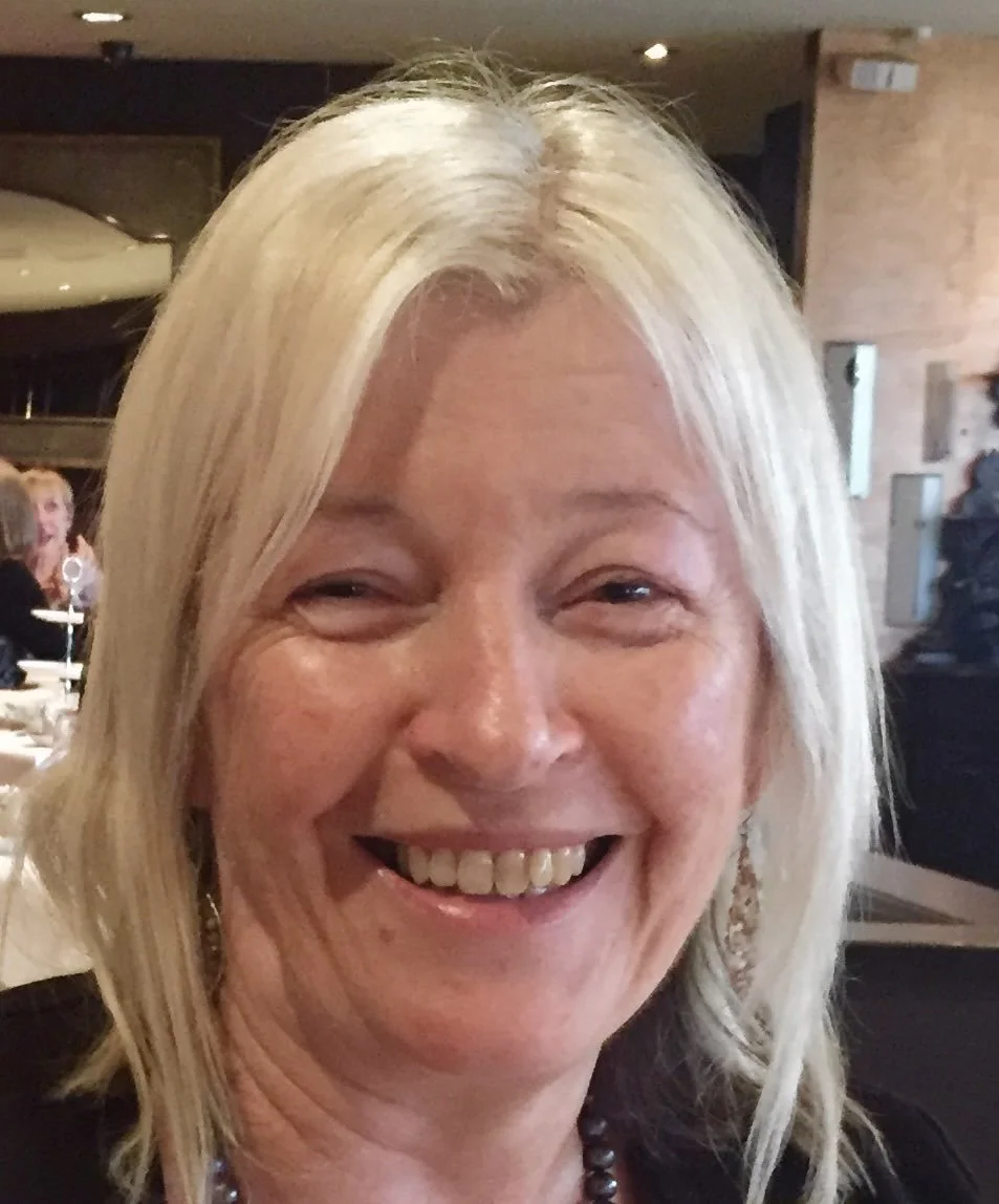 A woman with blonde hair smiling at a social gathering in a restaurant or event space.