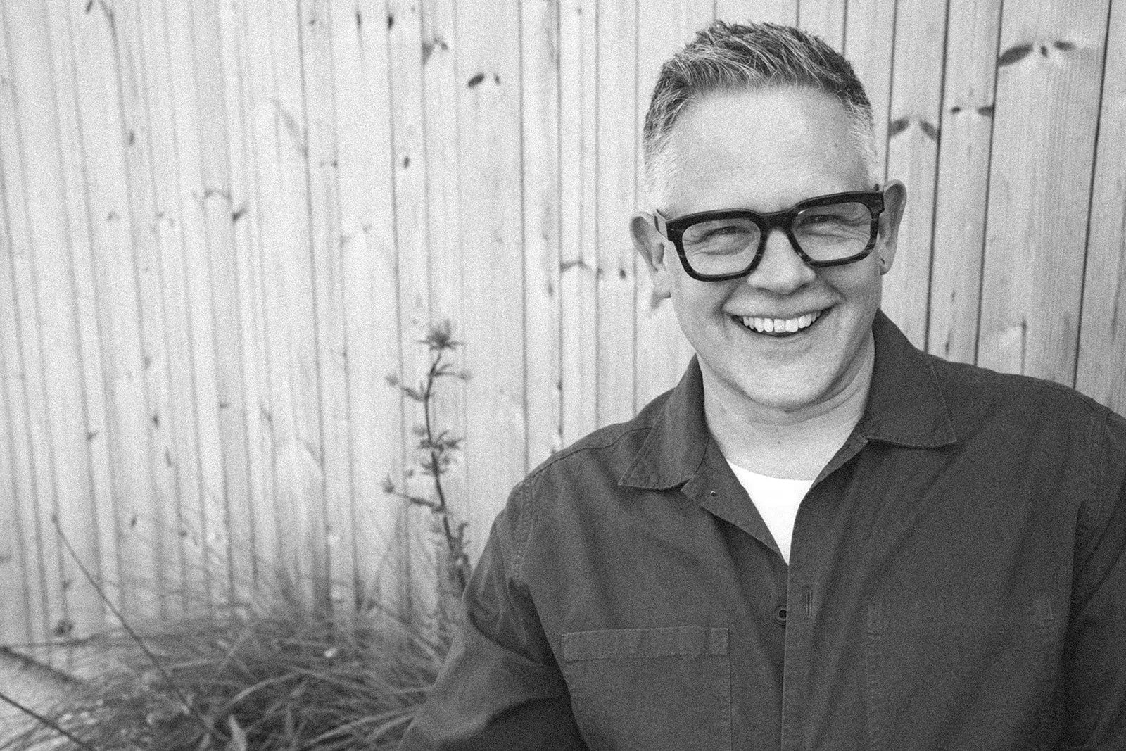 Mark Hardy Garden Designer smiling with glasses standing outdoors in front of a wooden fence.