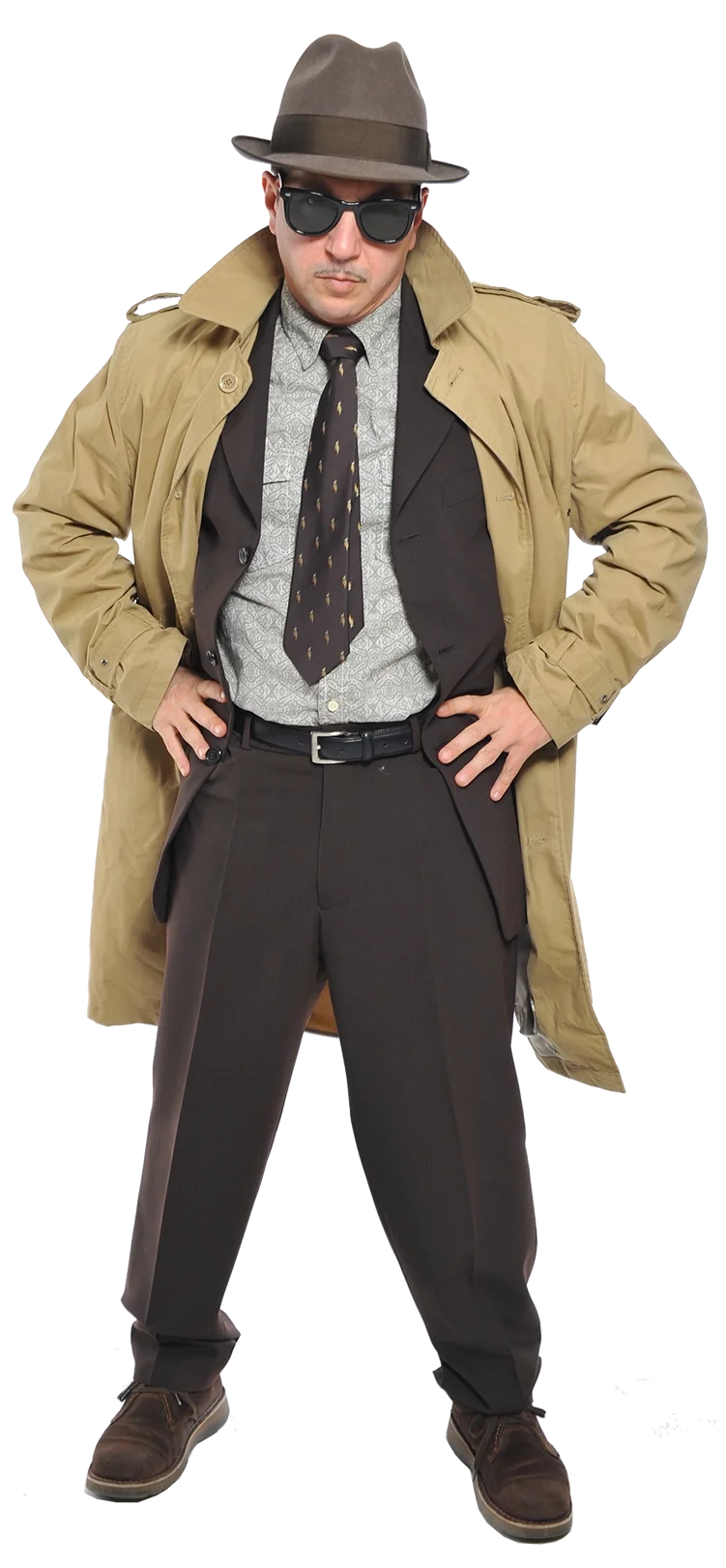 Ein komödiantischer Mann trägt einen Hut, Sonnenbrille, Trenchcoat, Anzug und Krawatte, steht mit Händen in den Hüften.