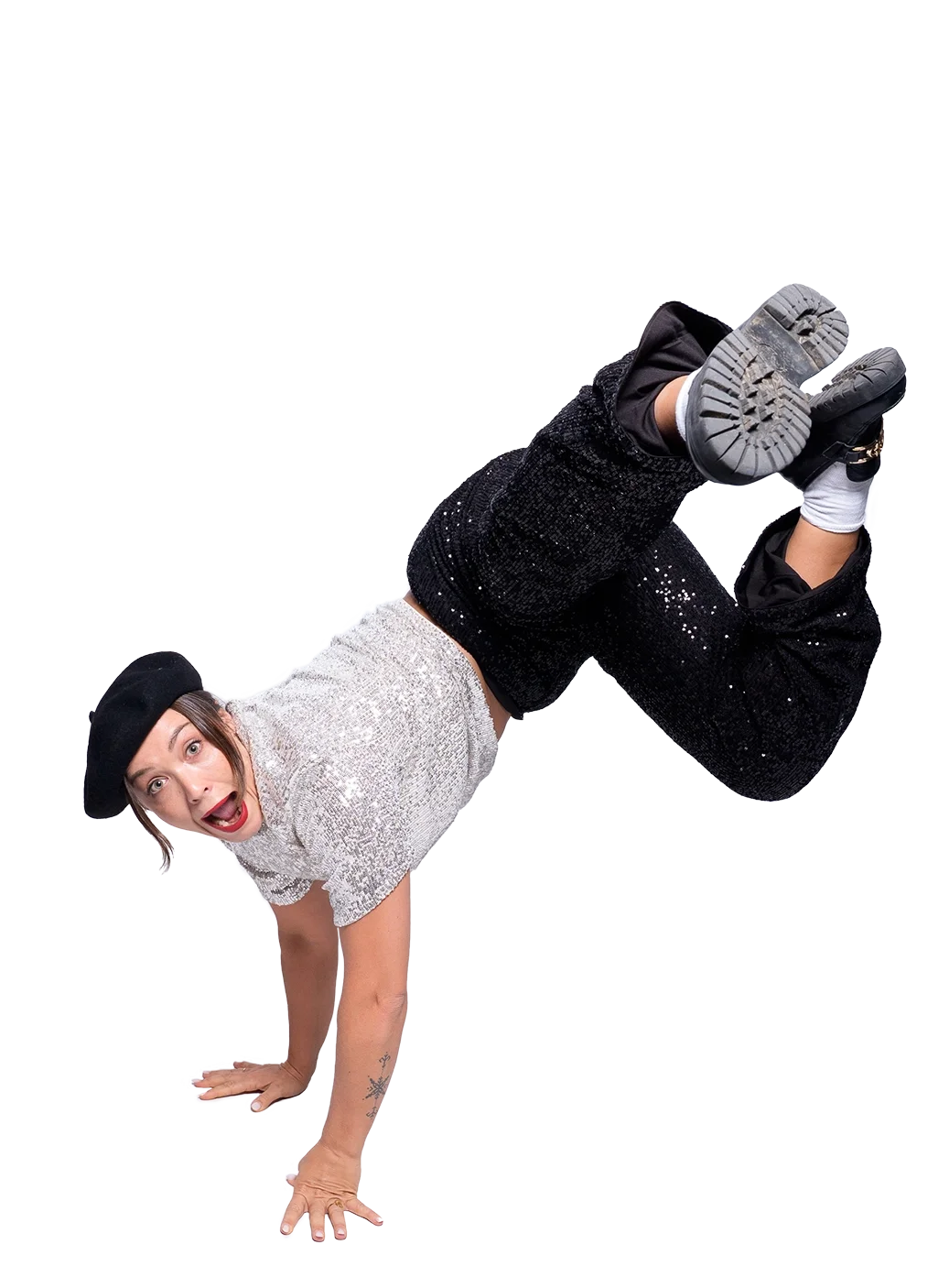 Eine Frau balanciert auf Händen mit einem Bein in der Luft, trägt einen schwarzen Hut und ein silbernes Top, lacht und wirkt lebhaft.