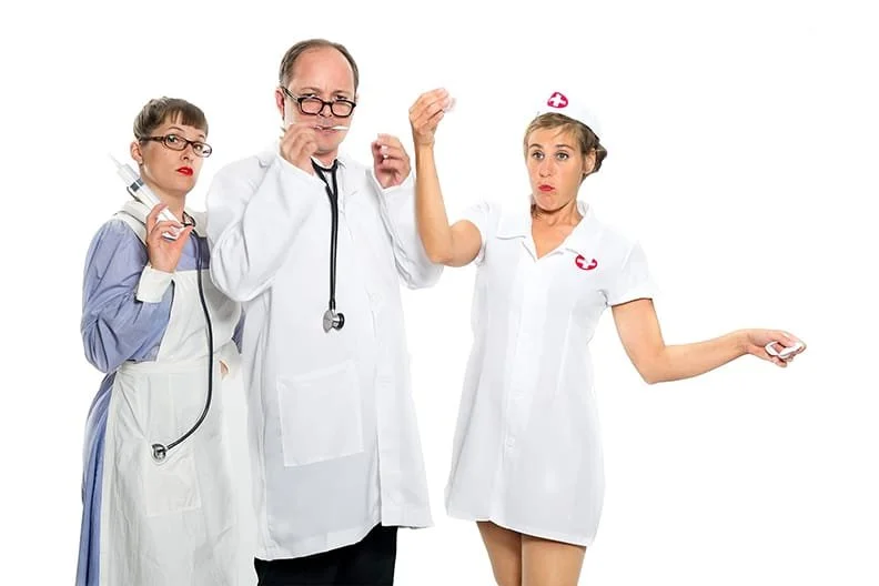Drei Personen in Arzt- und Krankenschwesterkostümen, die mit skeptischen Gesichtsausdrücken posieren, vor weißem Hintergrund.