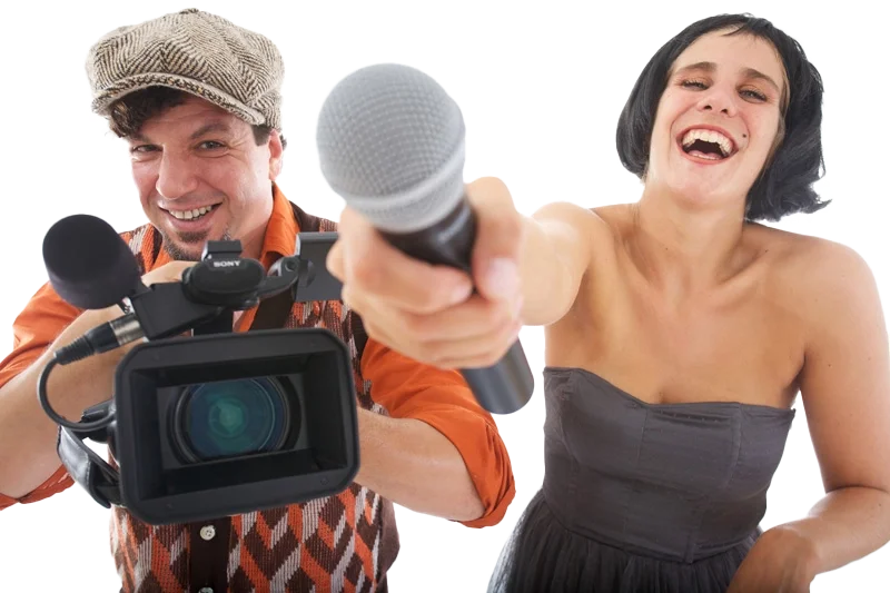 Ein Mann mit Peaky-Blinders-Hut und eine lachende Frau posieren mit Mikrofon und Kamera humorvoll.