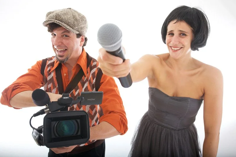 Ein Mann und eine Frau posieren mit Mikrofon und Kamera, lachen und scheinen für eine Aufnahme oder ein Interview bereit zu sein.