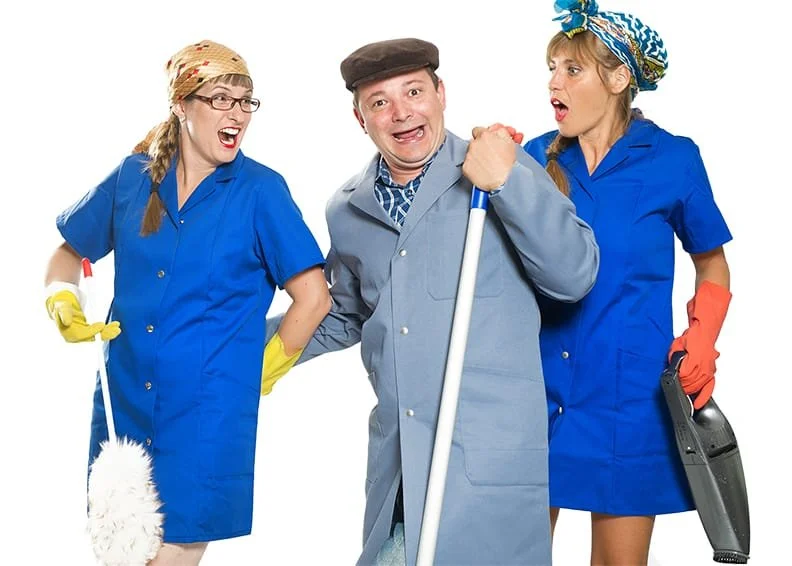 Drei Menschen in Putzuniformen und mit Reinigungsutensilien, lachen und posieren für die Kamera.