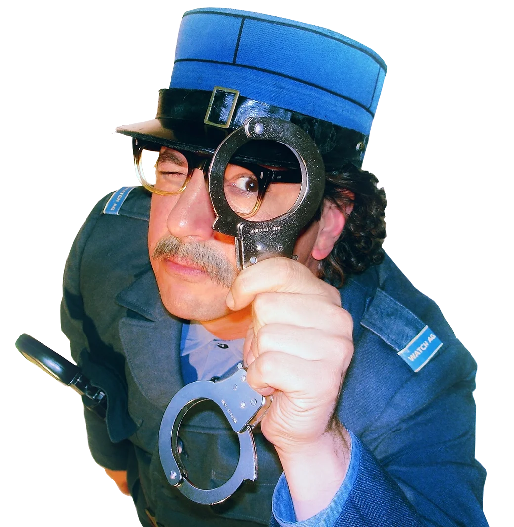 Ein komödiantischer Mann in Uniform mit Polizeimütze, Brille und Handfesseln hält eine Lupe vor einem Auge, als würde er etwas untersuchen.