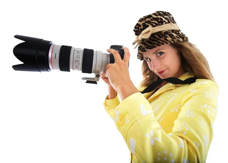 Frau mit gelbem Pullover und Leopardenmütze hält eine große professionelle Kamera mit Teleobjektiv