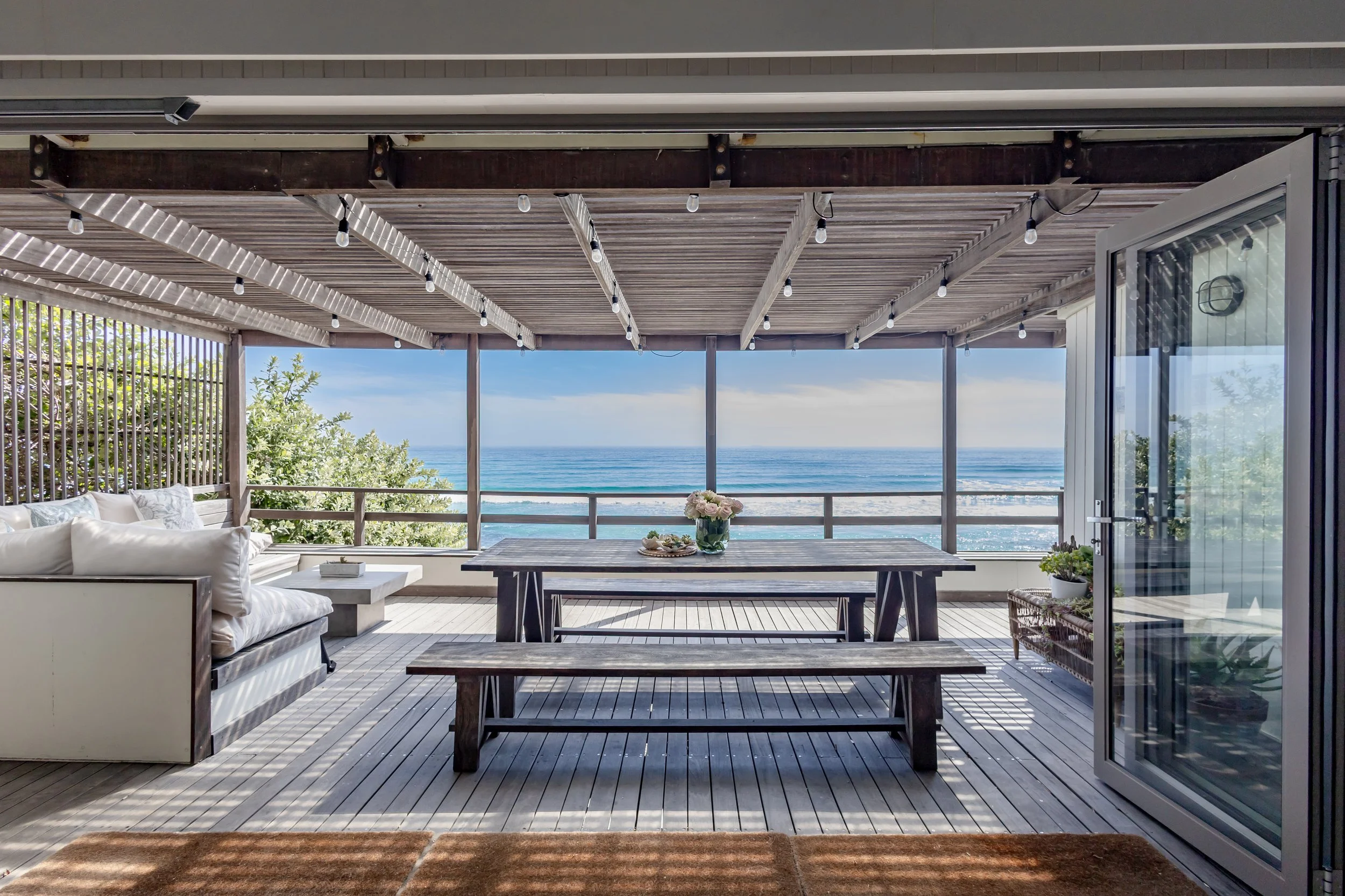 Wooden outdoor dining deck with a long bench table overlooking the Atlantic Ocean in Misty Cliffs.