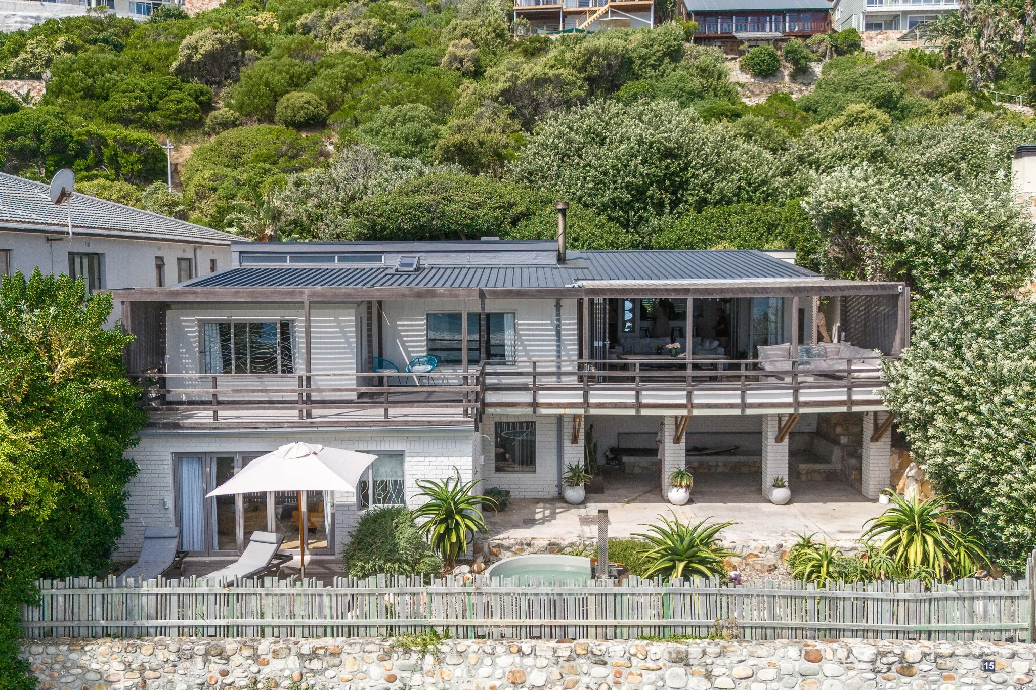 Two-story luxury beach house in Misty Cliffs, Cape Town, featuring white wood cladding and large glass windows.