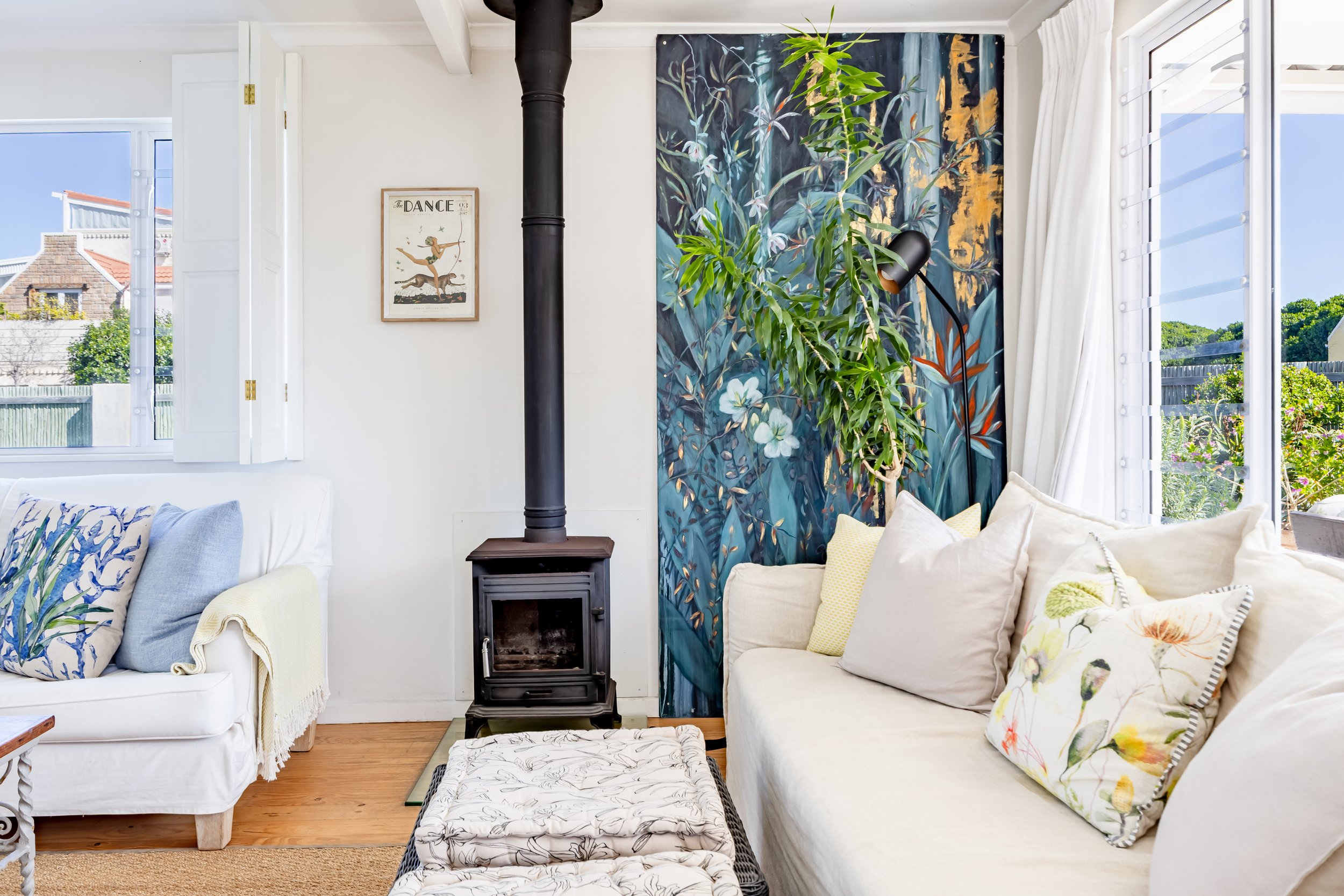 Light-filled coastal lounge featuring a wood-burning fireplace and colourful feature wall, captured for professional property photography in Cape Town.