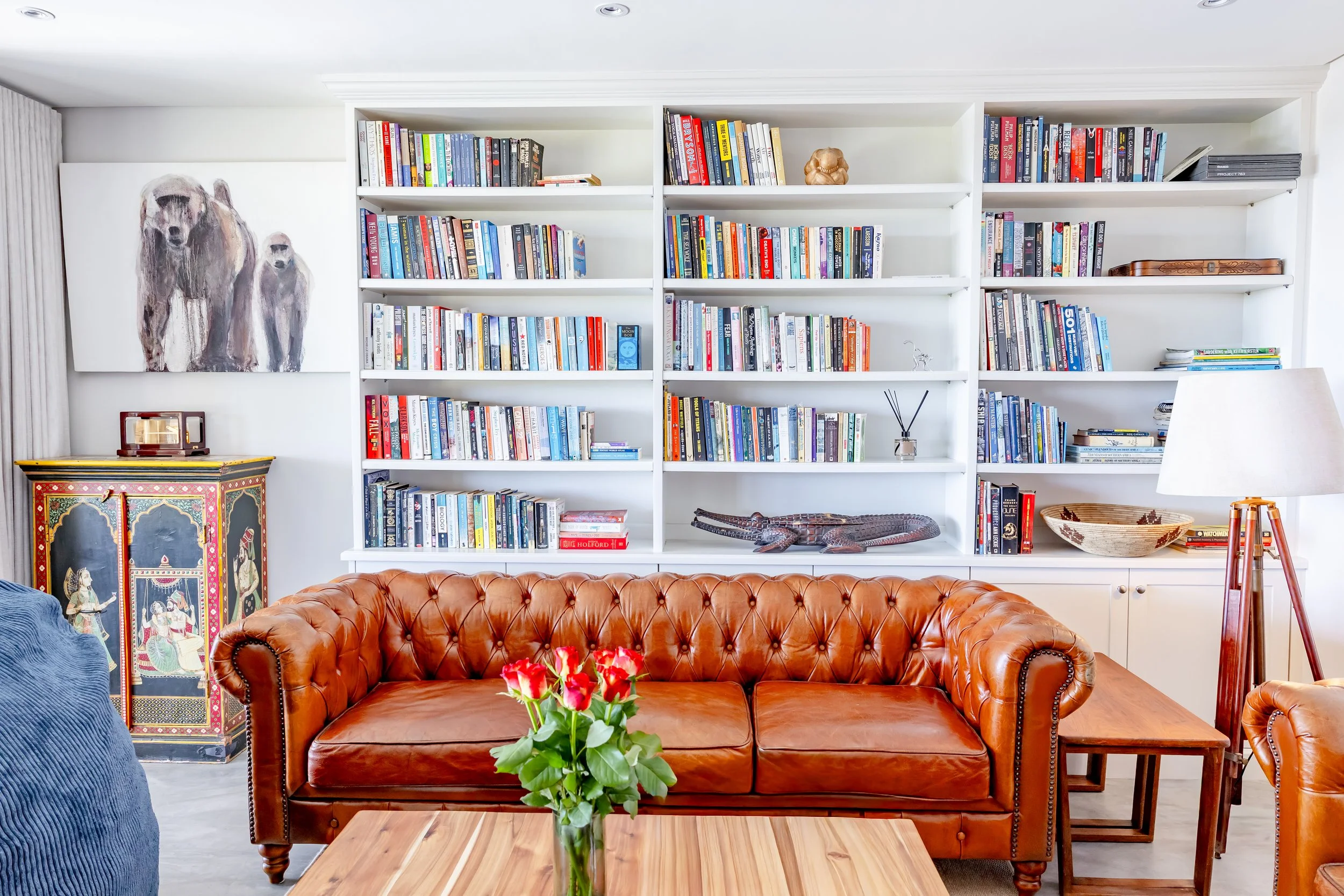Professional library photography in a Camps Bay home showing a classic brown leather Chesterfield sofa and floor-to-ceiling bookshelves.
