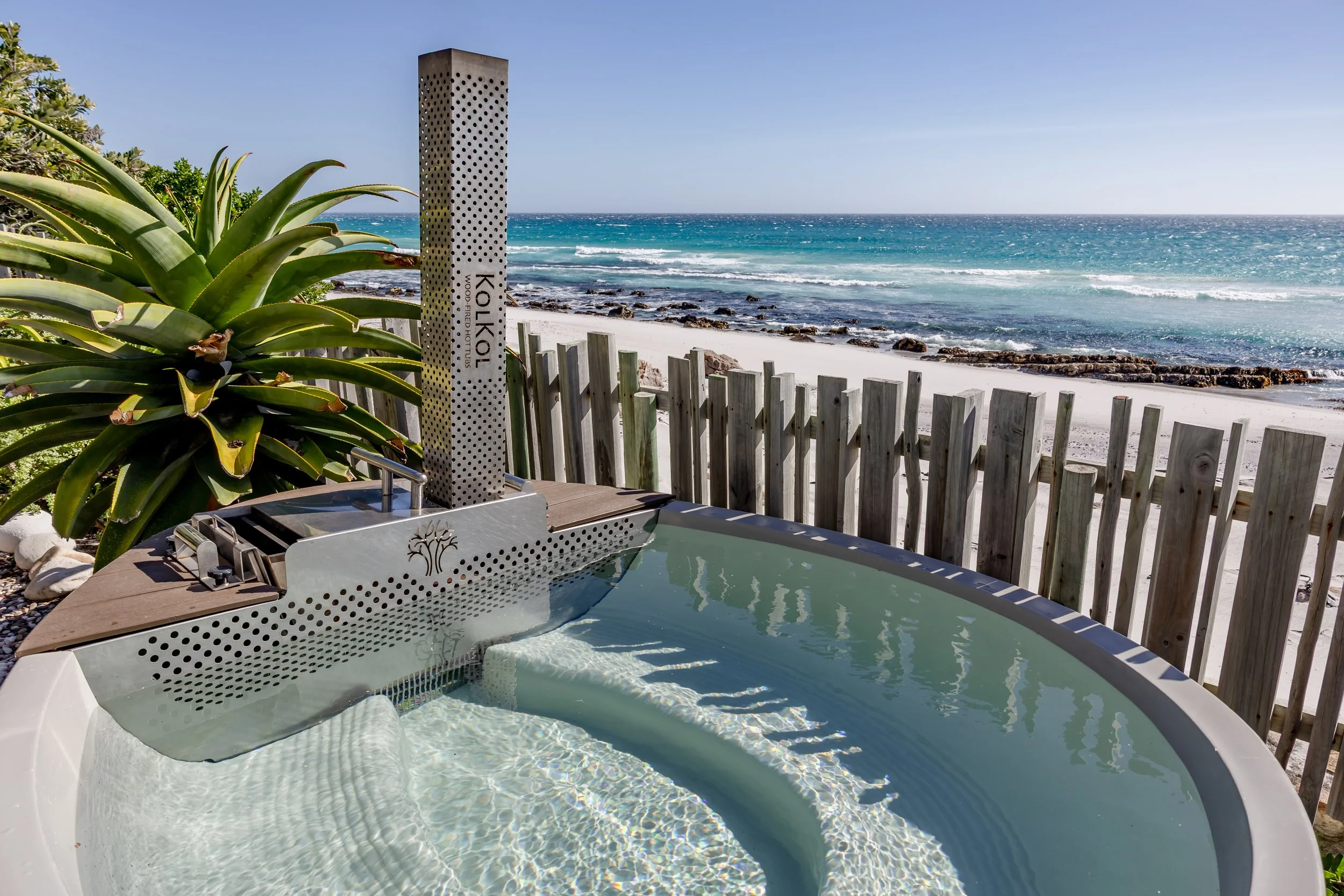 Private outdoor plunge pool and hot tub with a rustic wood fence overlooking the ocean waves.