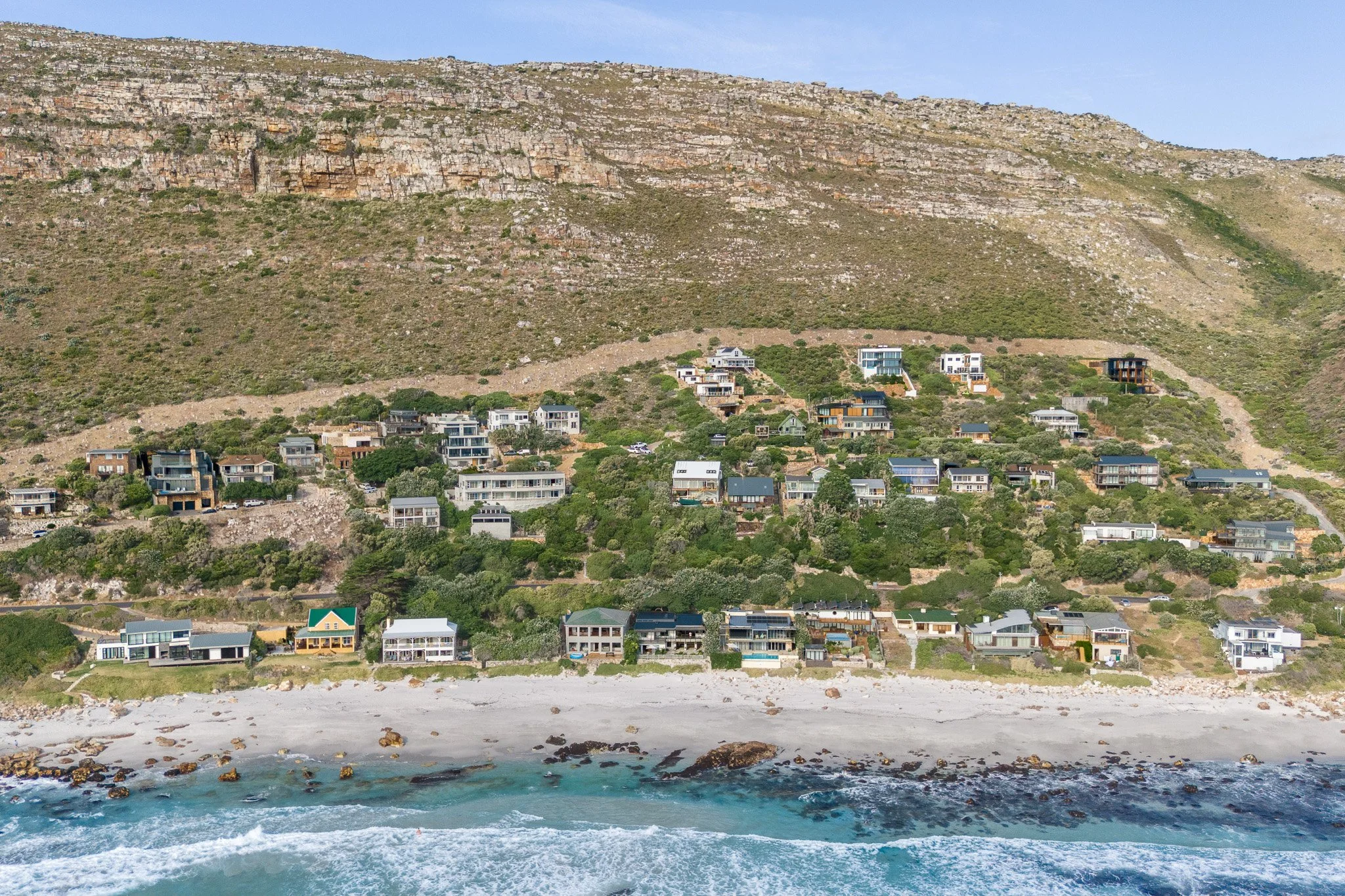 Aerial drone shot of a coastal holiday home nestled between the mountains and the beach in Misty Cliffs, South Africa.