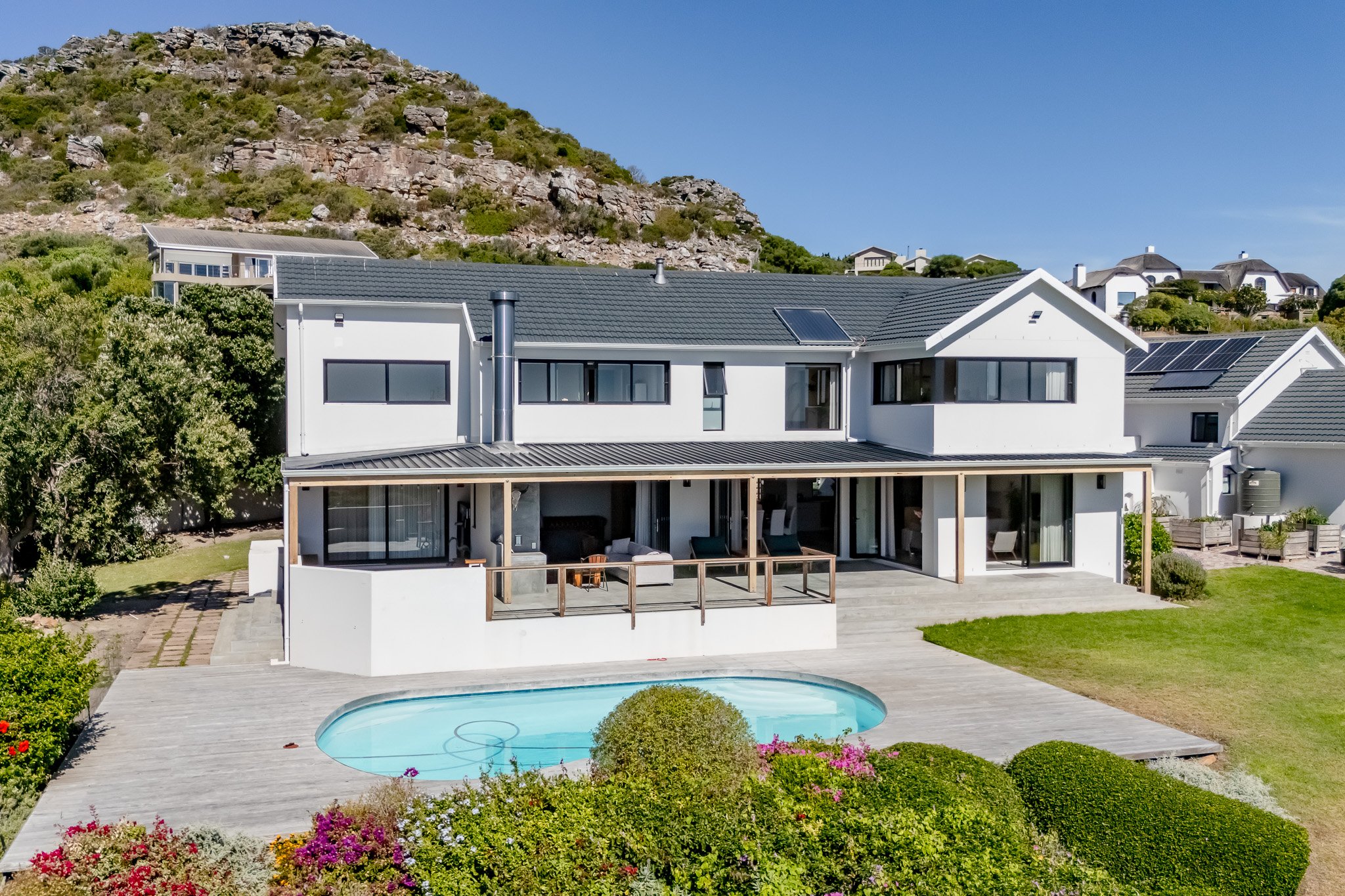 Real estate photography of a Constantia luxury estate showing a pristine swimming pool and modern white architecture against a mountain backdrop.