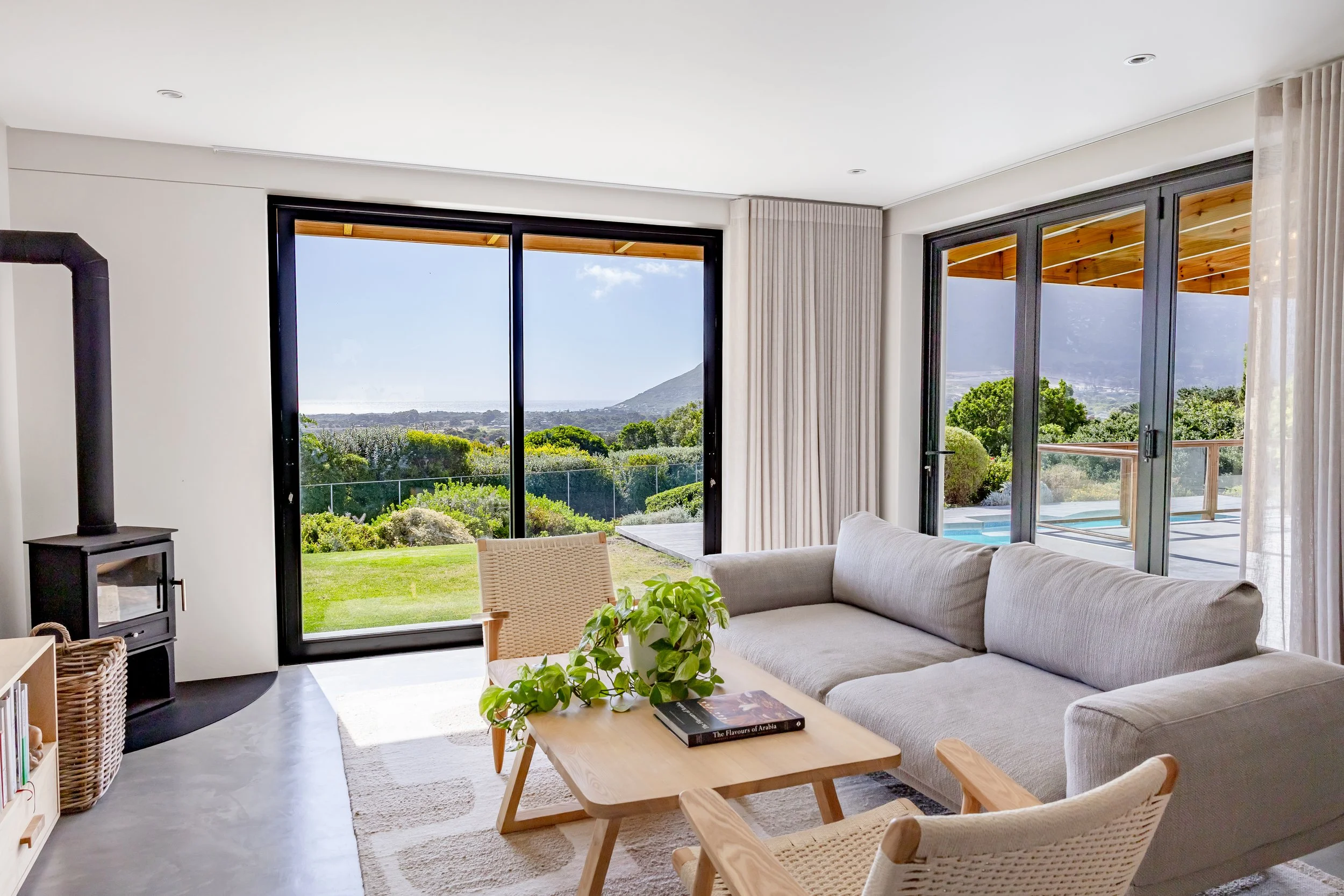 Luxury Noordhoek apartment living room with a large grey sectional sofa and floor-to-ceiling windows overlooking the Atlantic Seaboard.