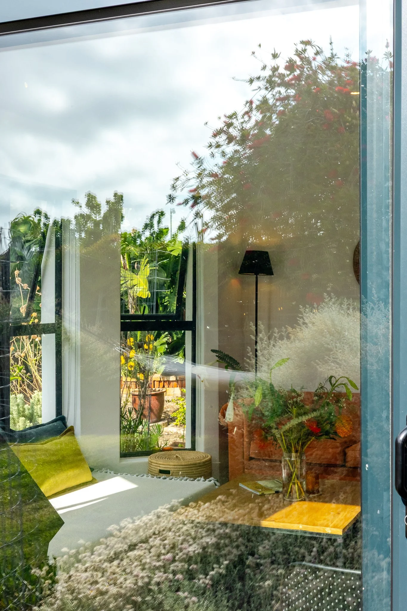 Artistic reflection shot on a glass door showing the interior of a Kommetjie property blending seamlessly with its natural garden surroundings.
