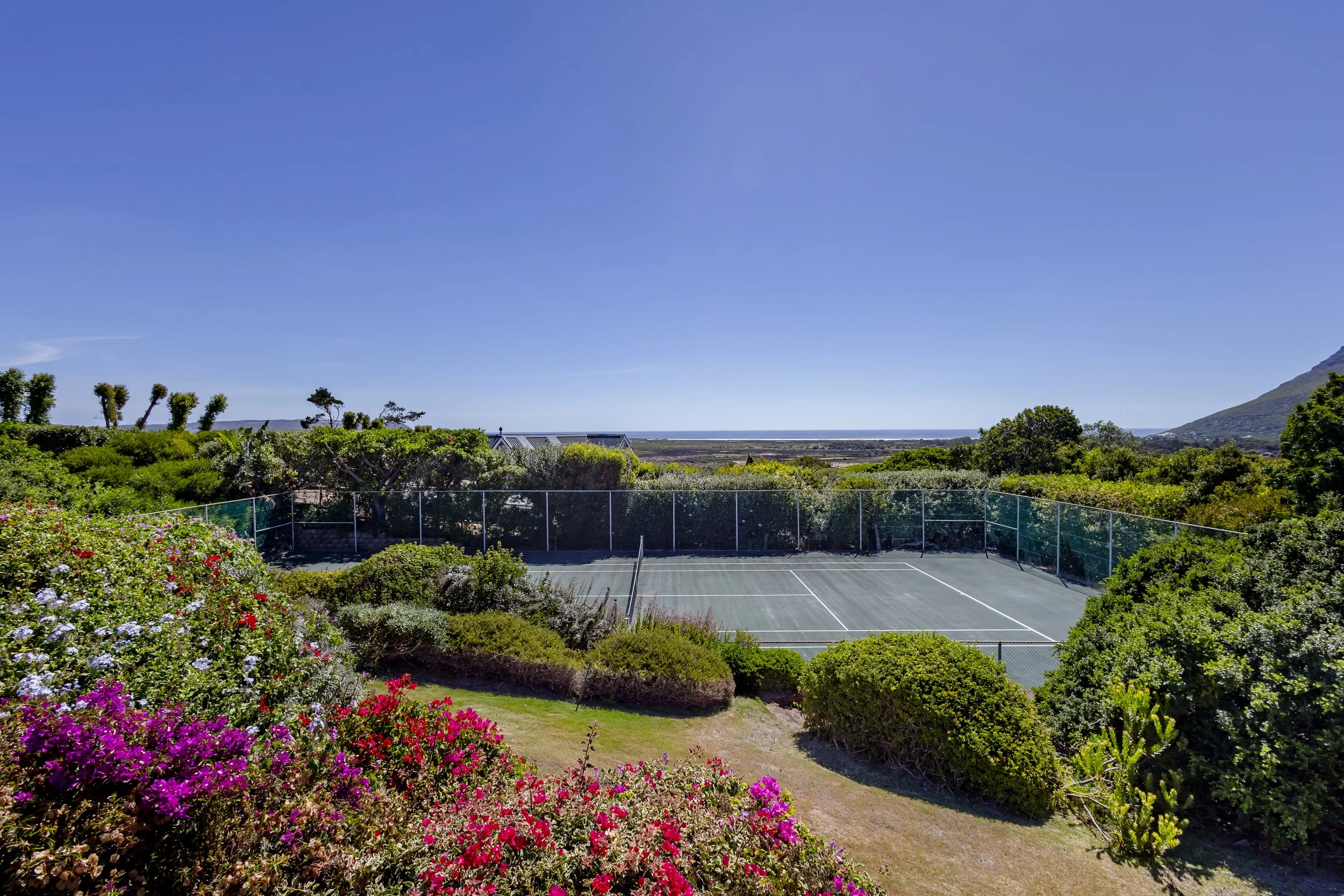 Wide-angle photography of a private tennis court and lush gardens at a premier Camps Bay accommodation.