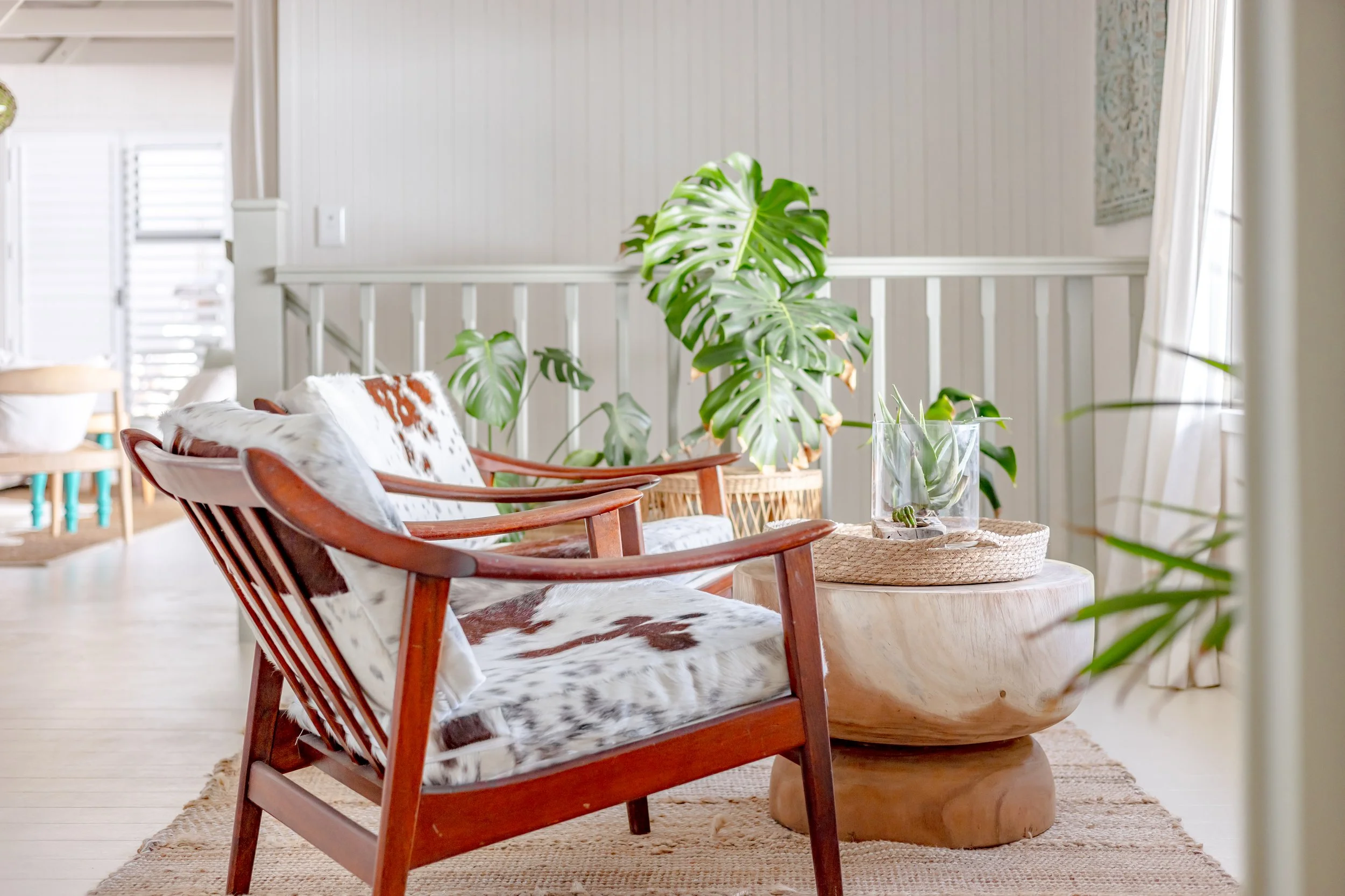Close-up of a stylish armchair with cowhide upholstery and a lush Monstera Deliciosa plant in a coastal villa.