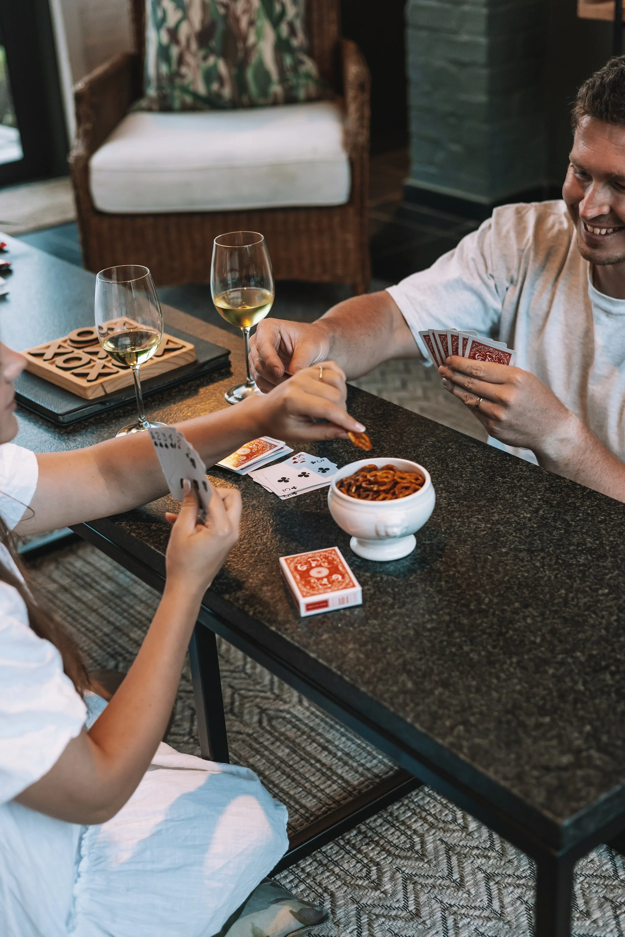 Two people playing card games at a table with snacks and wine in a cozy indoor setting.