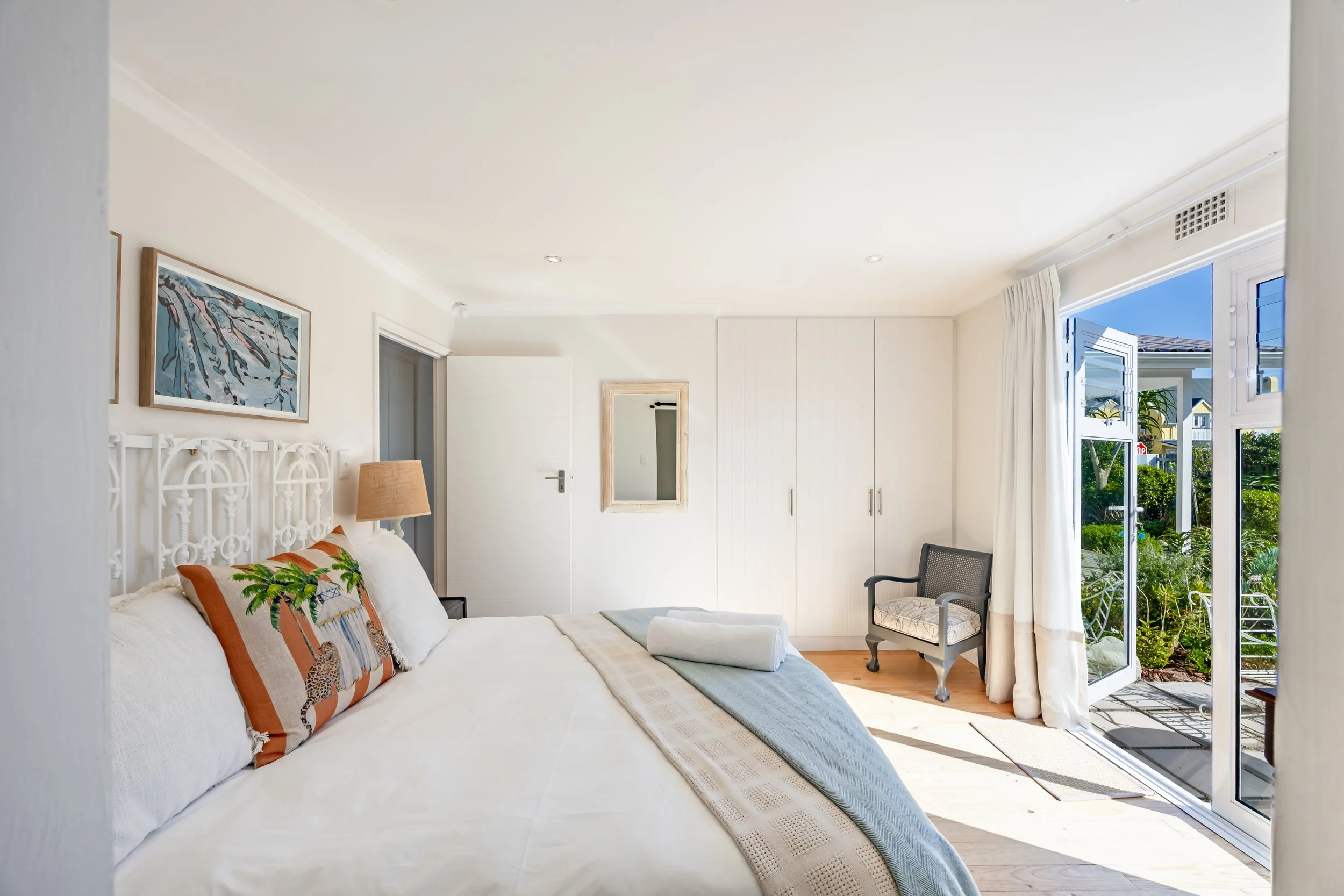 Bright coastal-style bedroom with natural light, soft furnishings and garden views, photographed for an Airbnb accommodation in Cape Town.