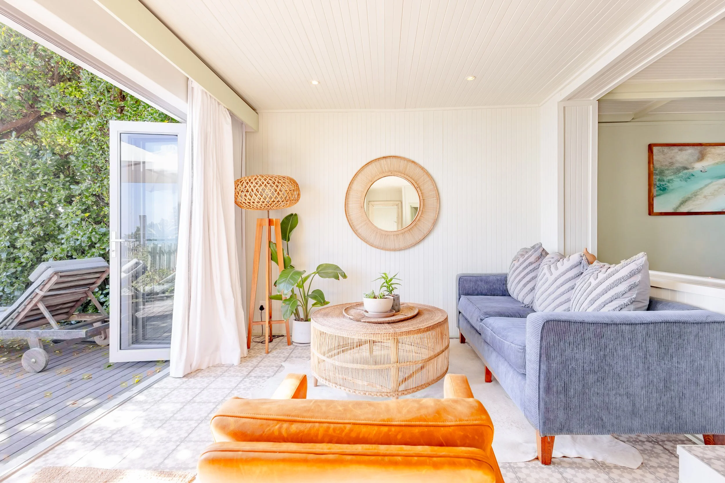 Bright indoor-outdoor sunroom with a vibrant orange velvet chair and a circular wooden coffee table.